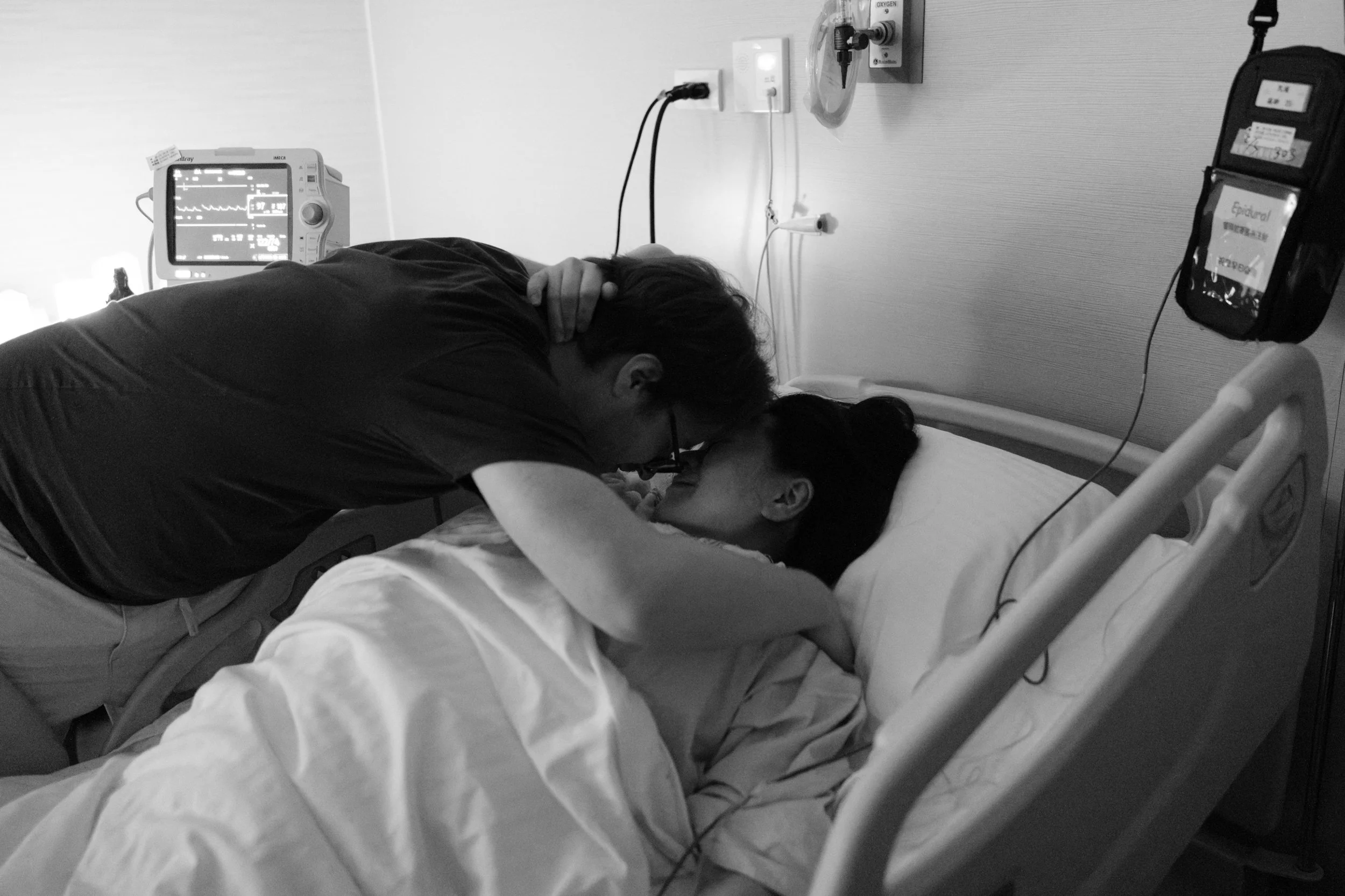 C-section birth photography at Dianthus Taipei — partner and mother share a kiss in the hospital bed after delivery.
