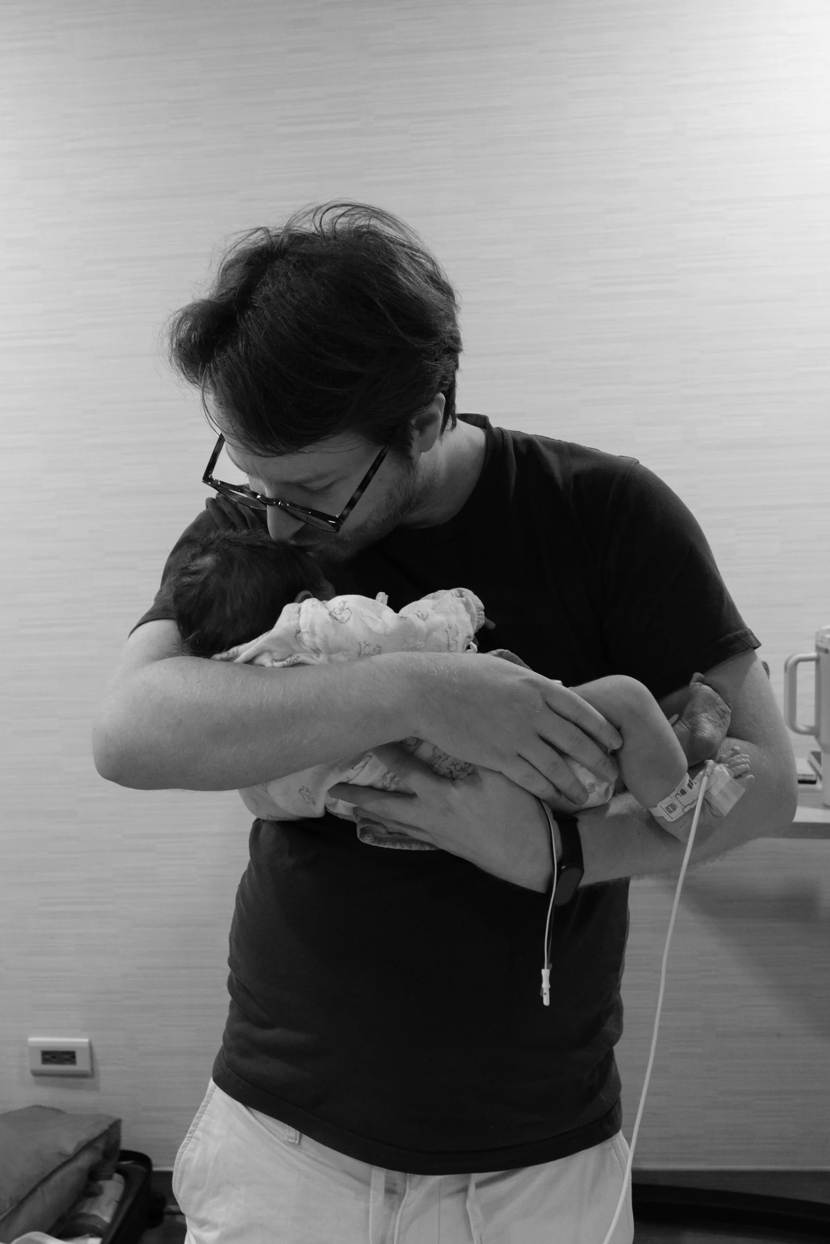 Birth photography at Dianthus Taipei — father tenderly holding his newborn baby in the hospital room.