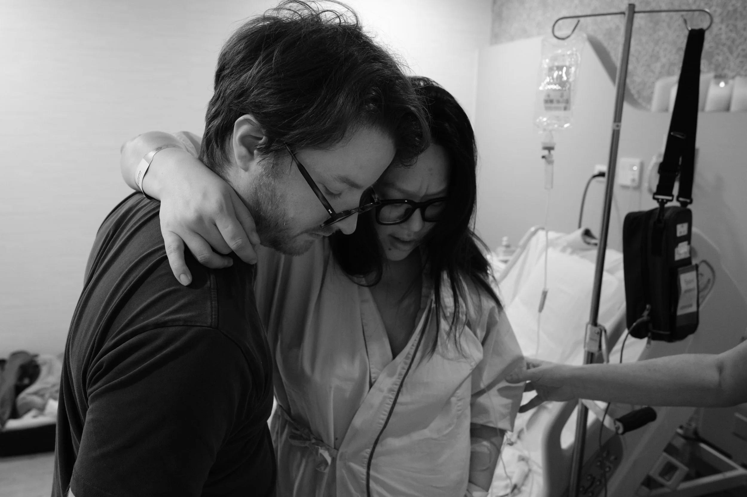 Documentary birth photography at Dianthus Taipei — partner embraces mother as she walks after surgery, arm around his shoulder.