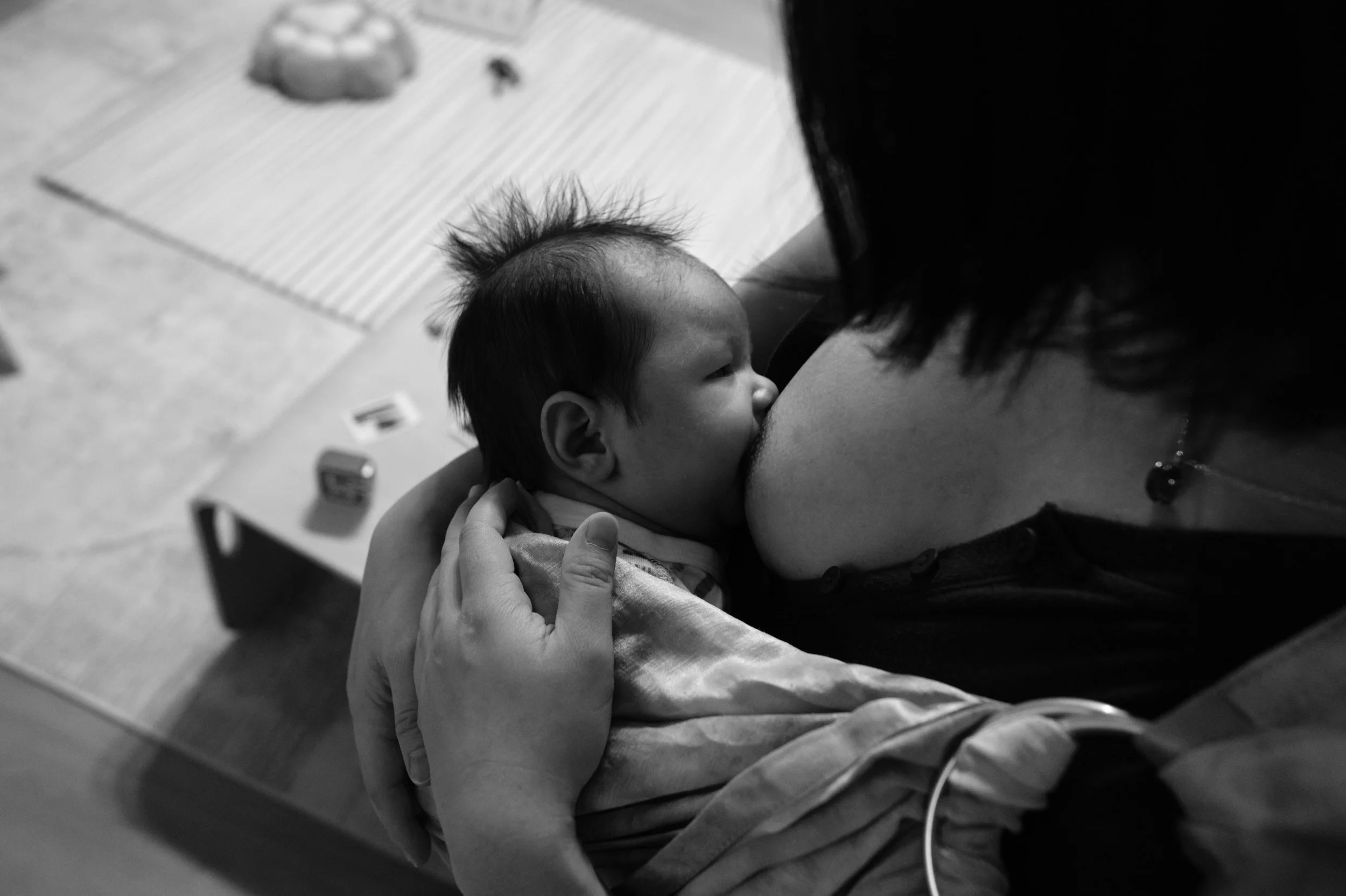 Close-up overhead black and white photo of a mother breastfeeding her newborn, her hand supporting the baby's back.