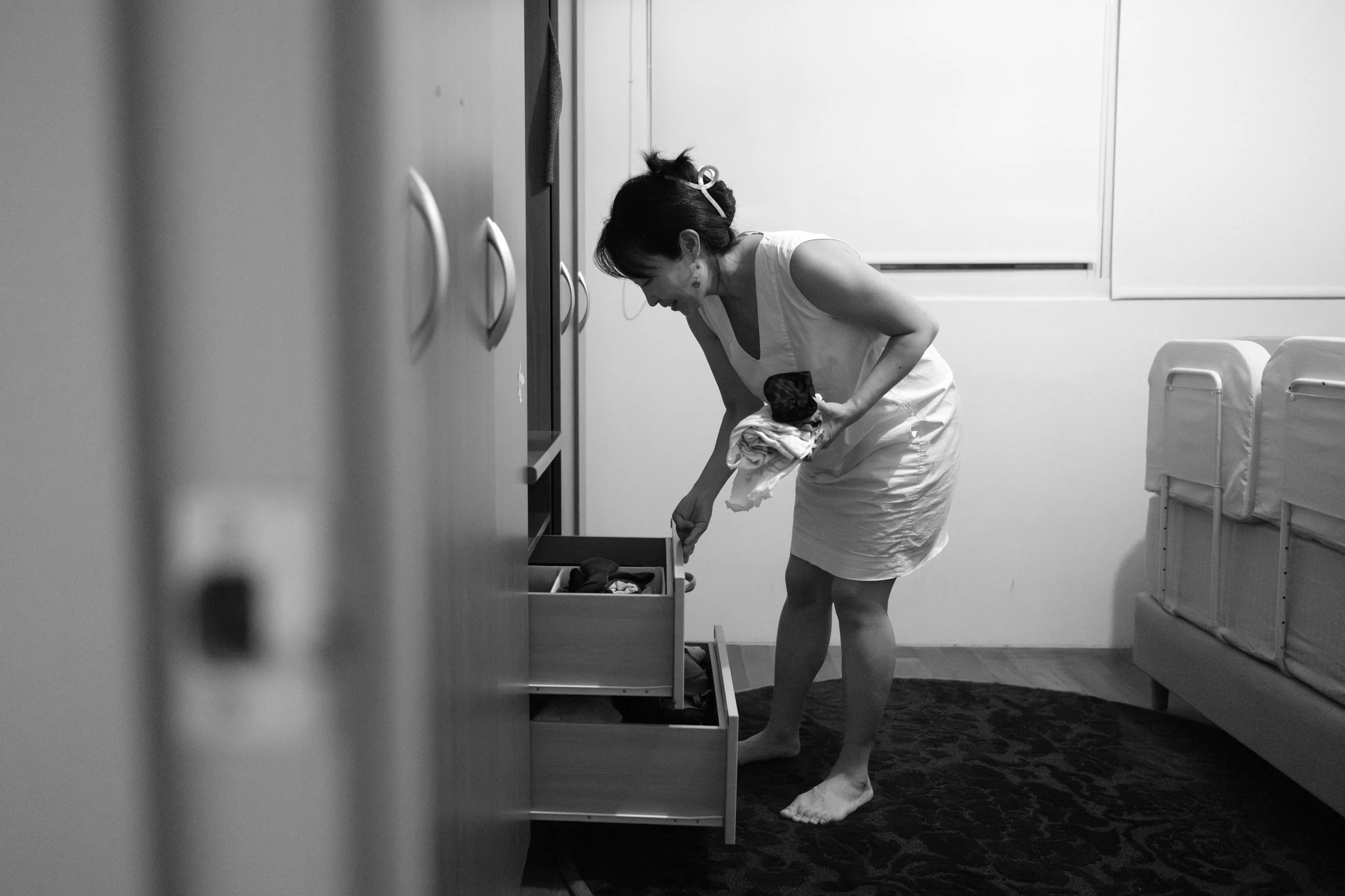 Candid documentary photo from a Taipei family photoshoot showing a mother getting pajamas from a dresser drawer during the bedtime routine.