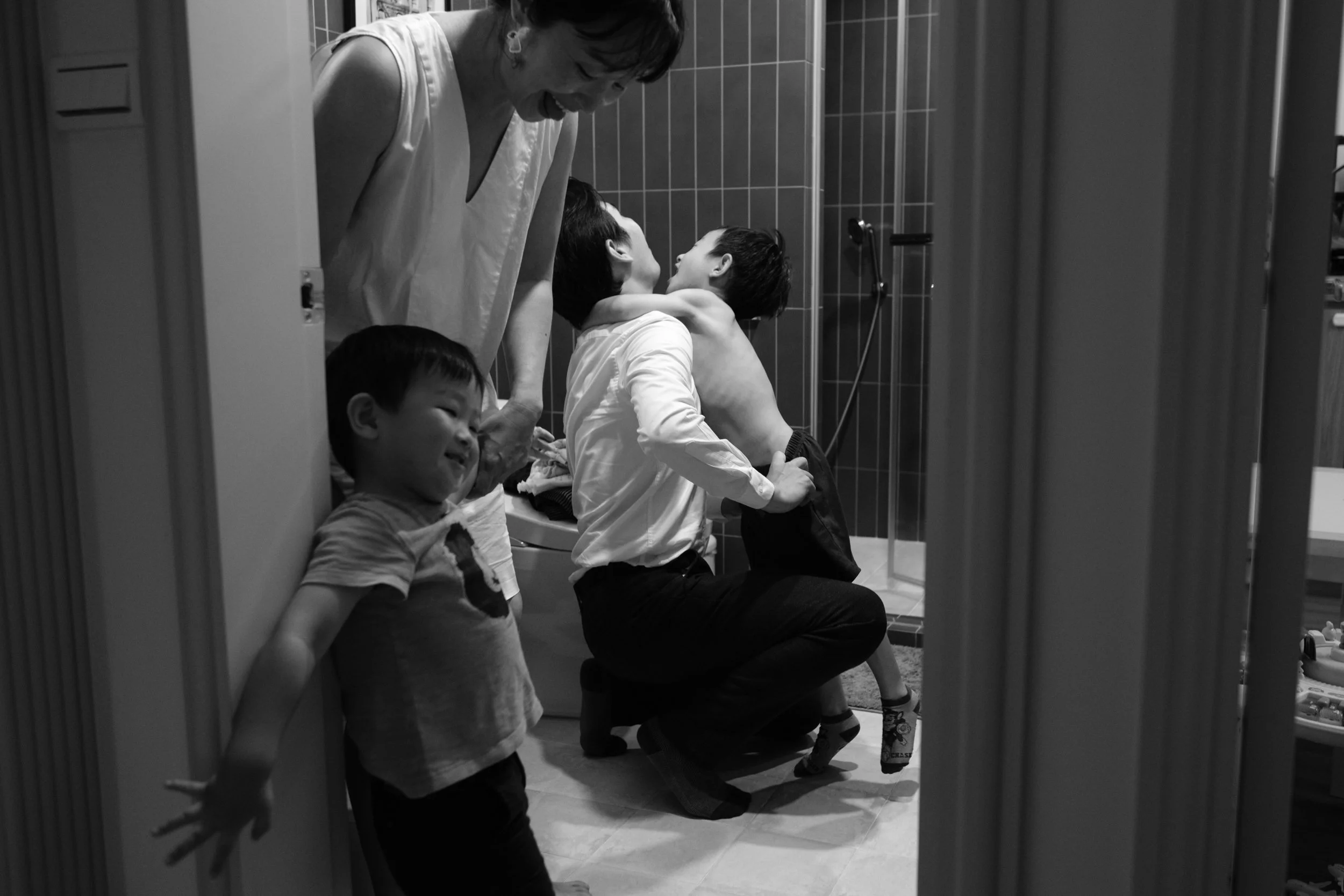 At-home family photography session in Taipei capturing a father hugging his shirtless son in the bathroom doorway during bath time.