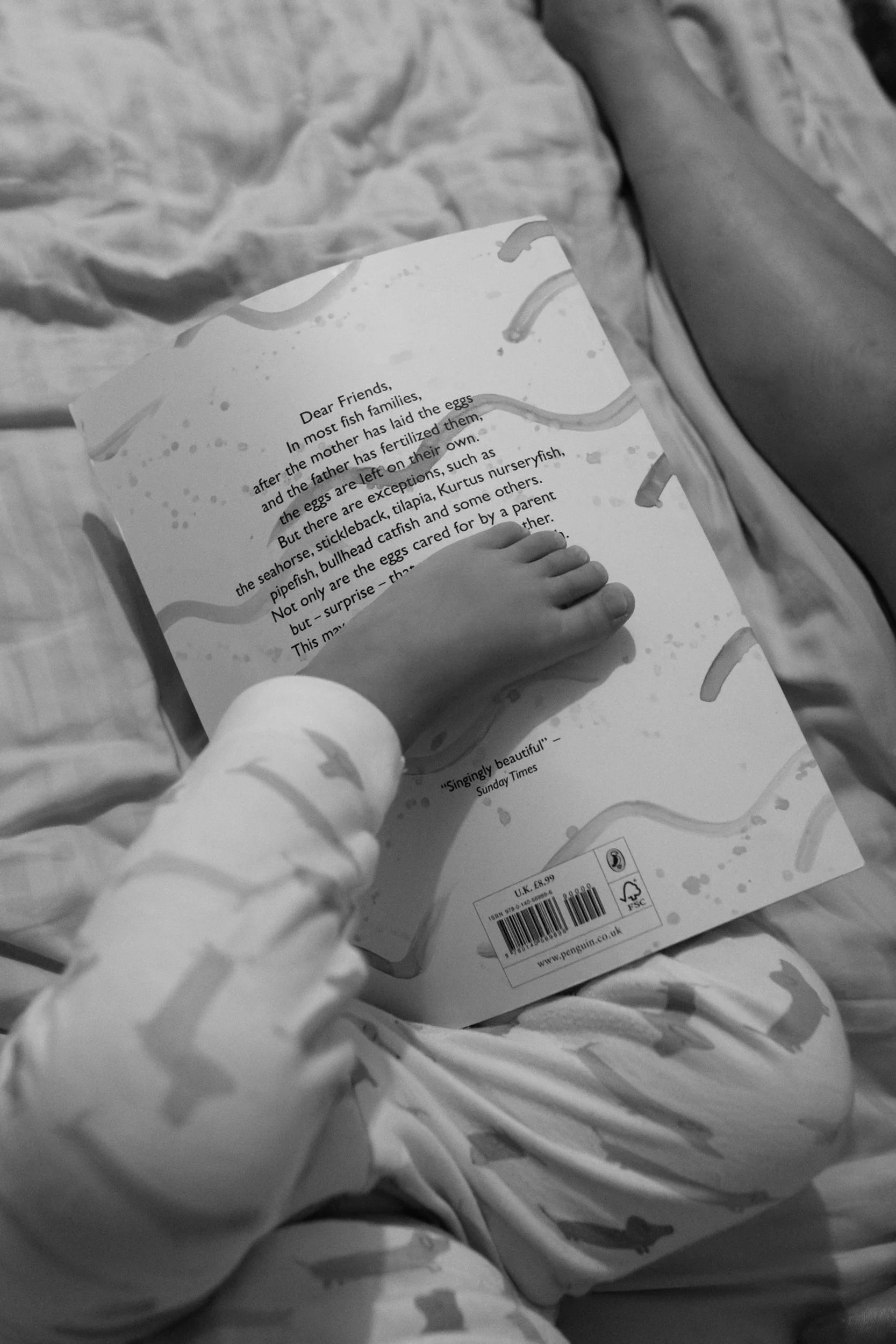 Documentary bedtime photo from a Taipei family photography session, close-up of a child's foot resting on an open picture book.