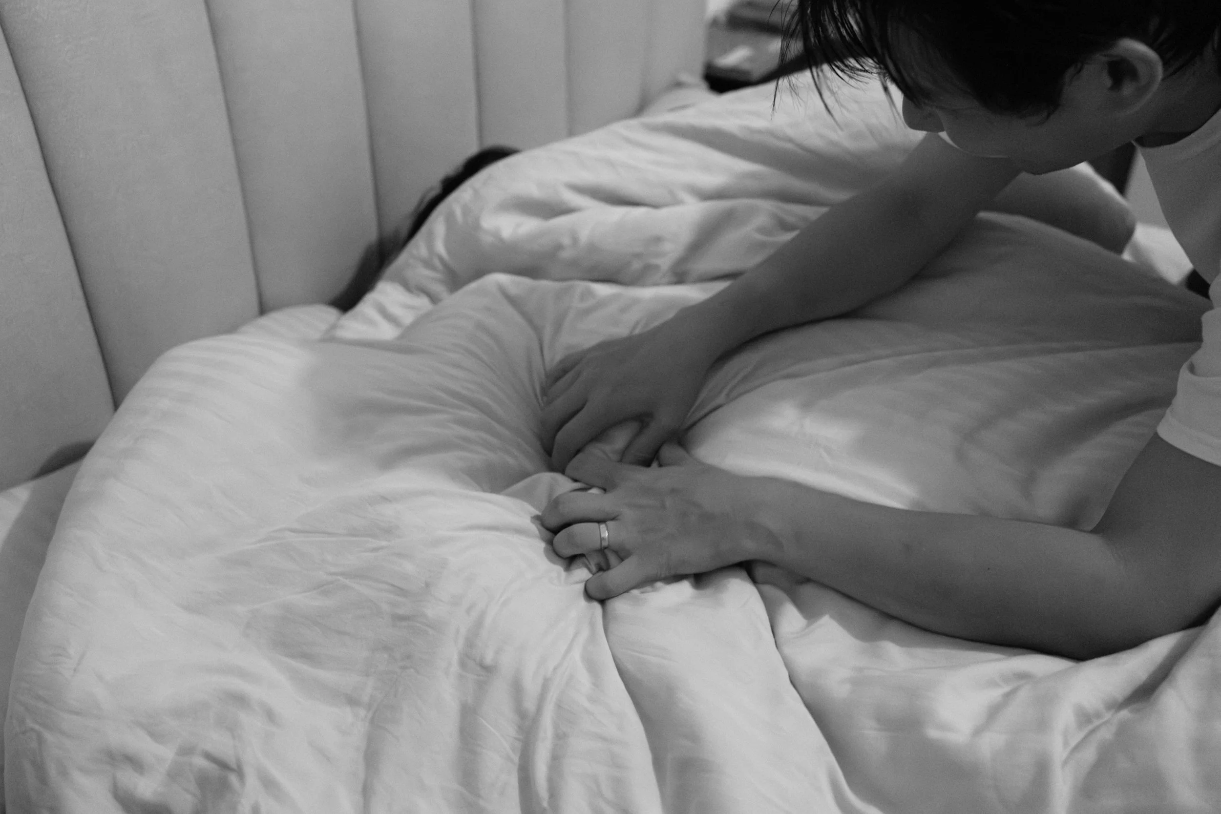 Candid documentary photo from an at-home Taipei family photoshoot, father tucking his child into bed at night.