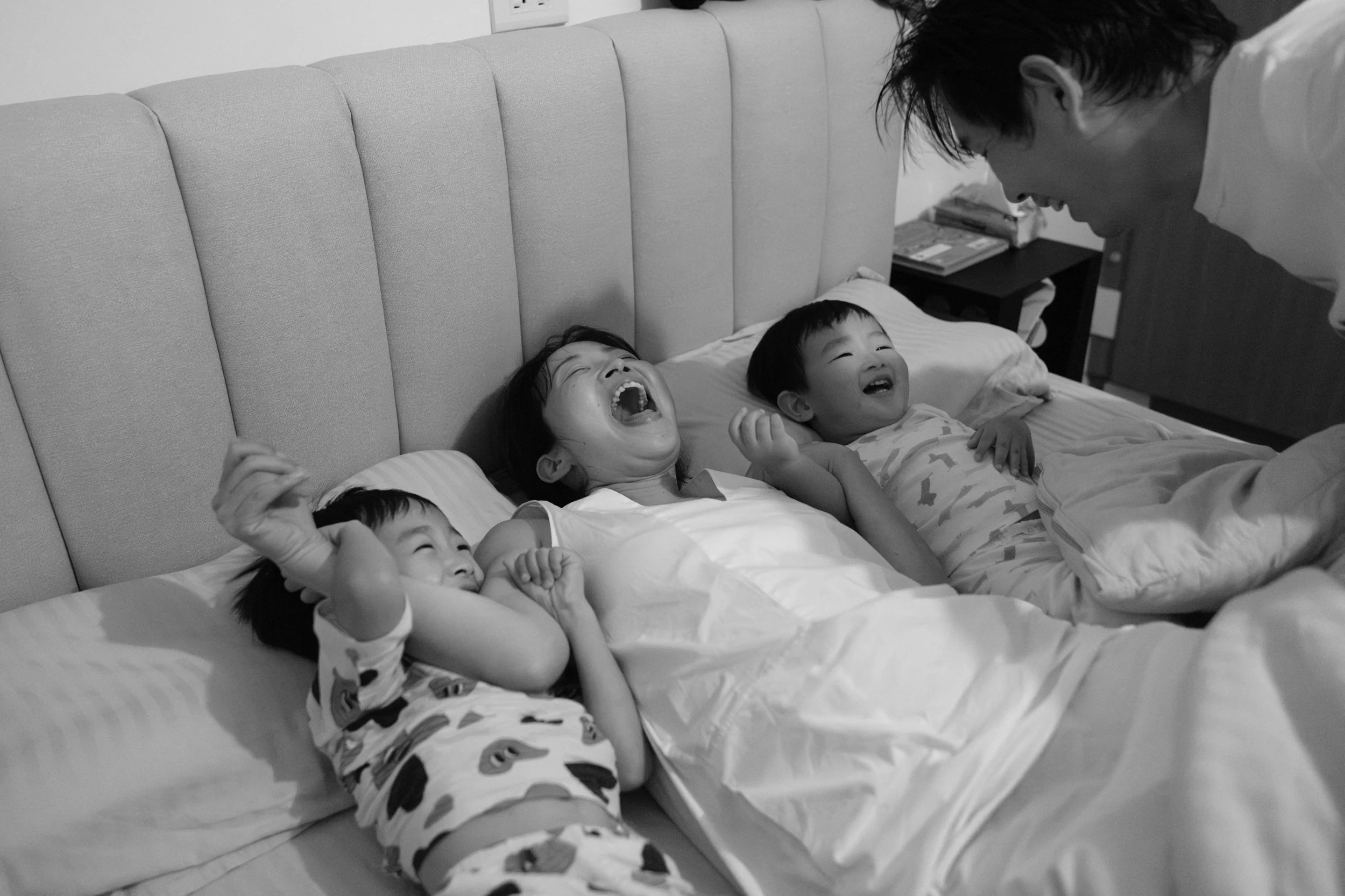 Documentary family photography in Taipei capturing a mother laughing in bed between her two sons during the bedtime routine.