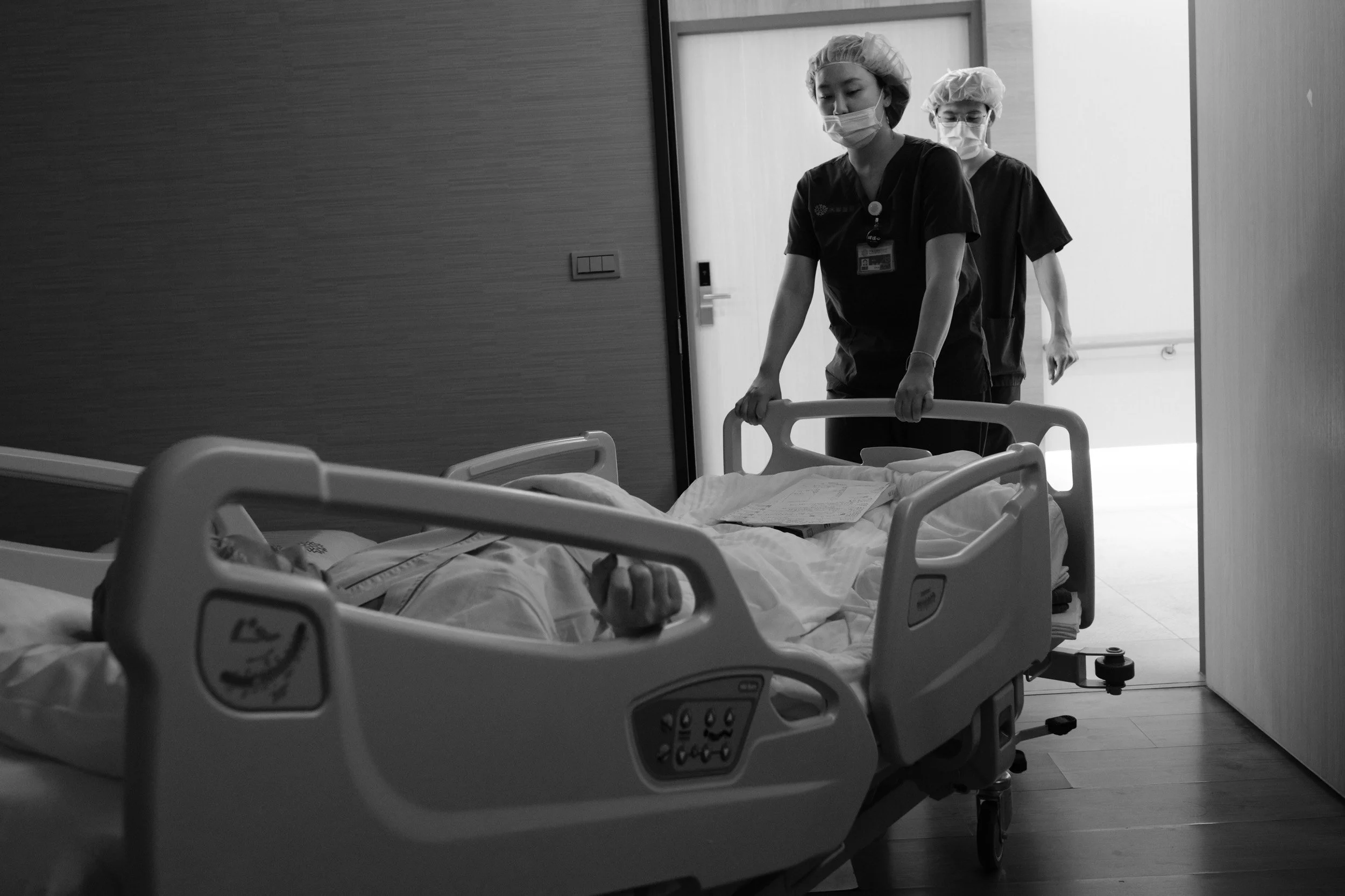 Two nurses wheel the mother's hospital bed toward the operating room, a birth photographer's documentary image at Dianthus in Taipei