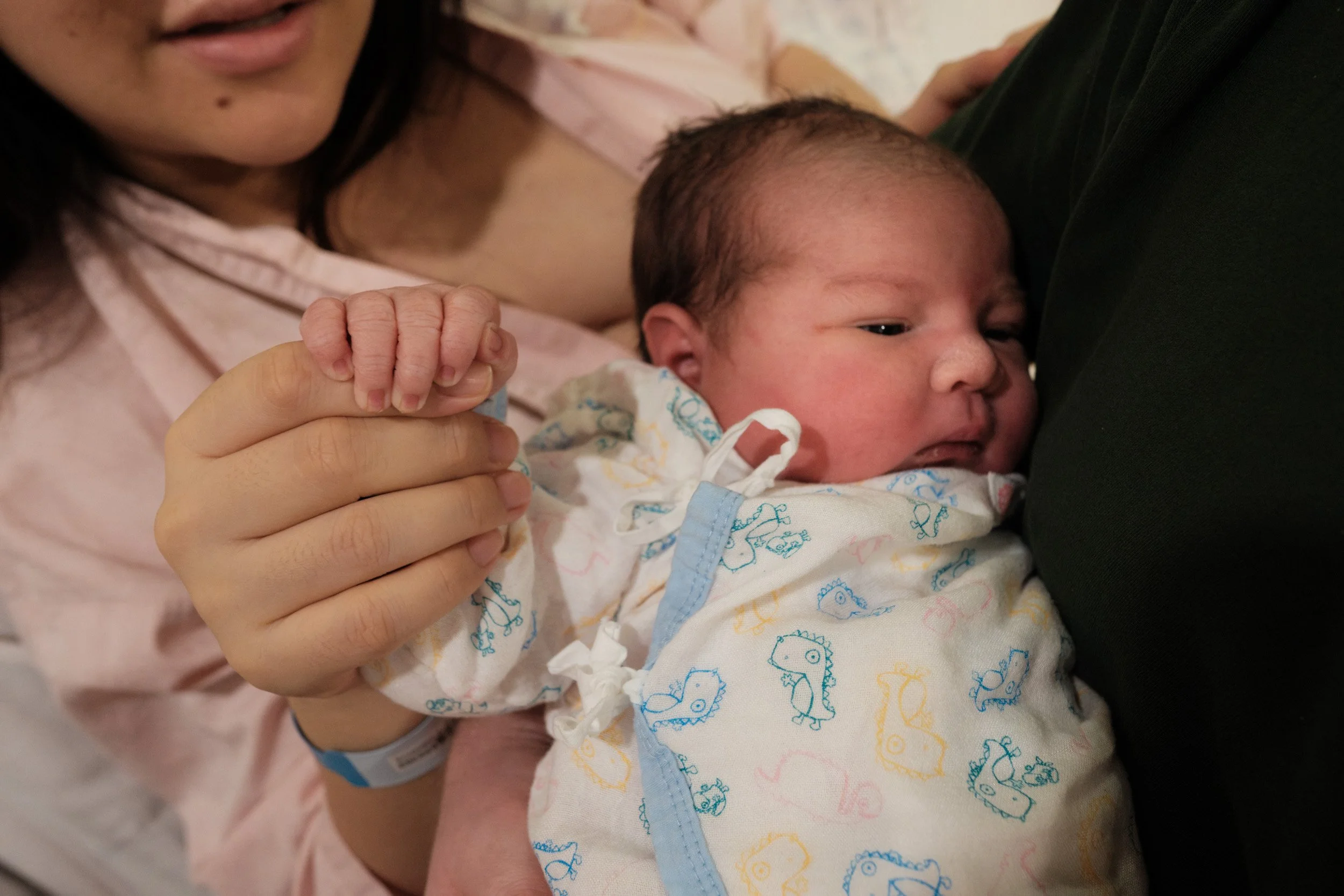 Newborn in a dinosaur-print wrap grips his mother's finger during a fresh 48 session by a Taipei birth photographer at Dianthus