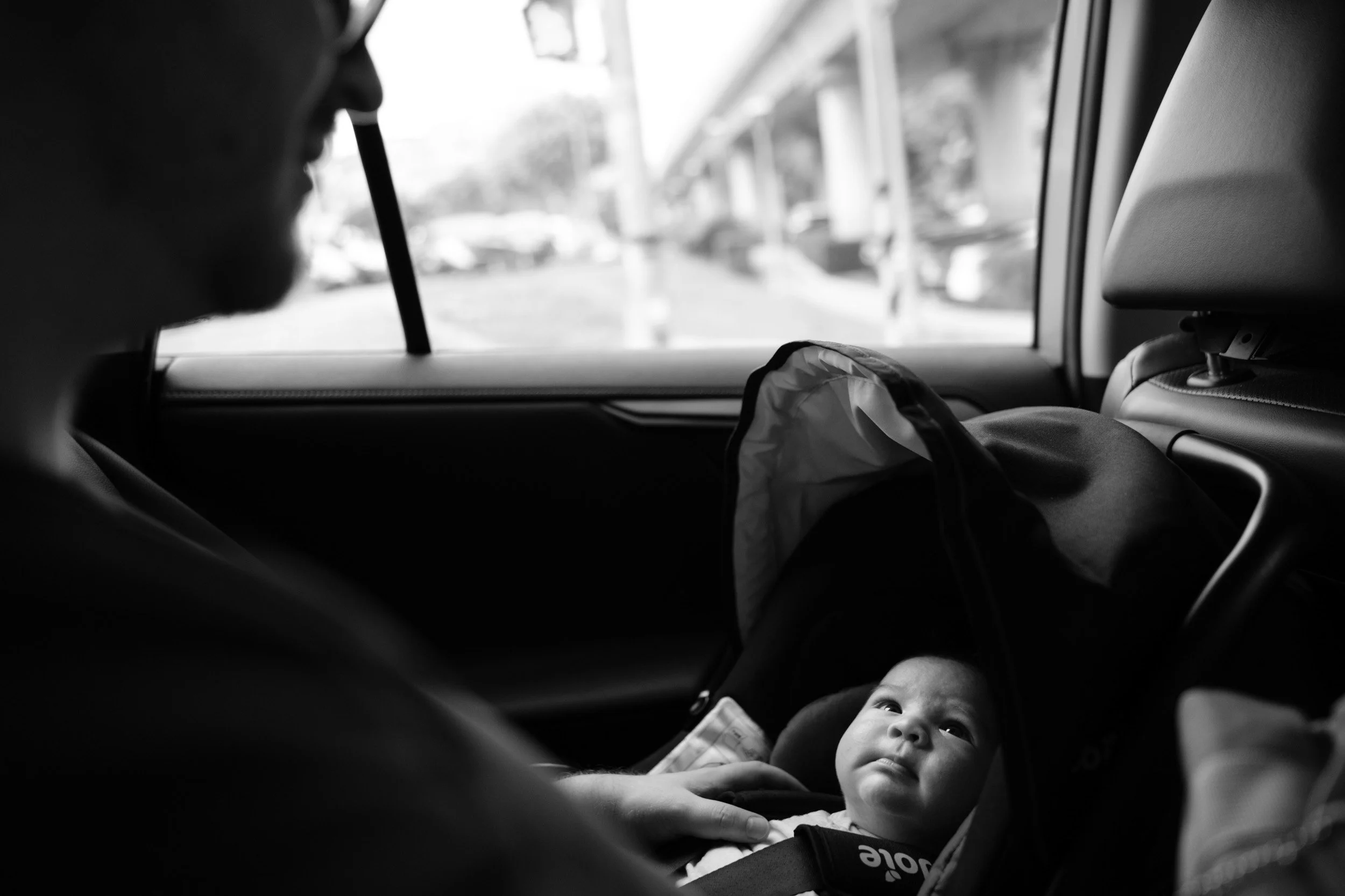 Father rests his hand on his newborn's chest in a car seat during the ride home from Dianthus, a Taipei newborn homecoming session