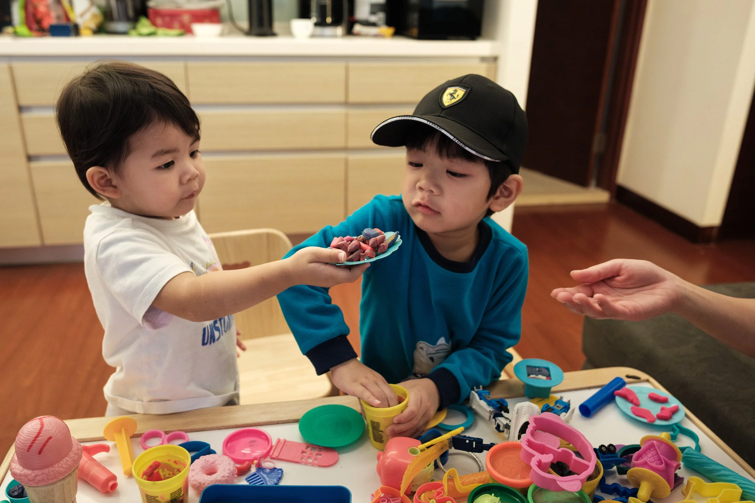 Two toddlers share play dough at a table during a documentary family photography session in Taipei, Taiwan