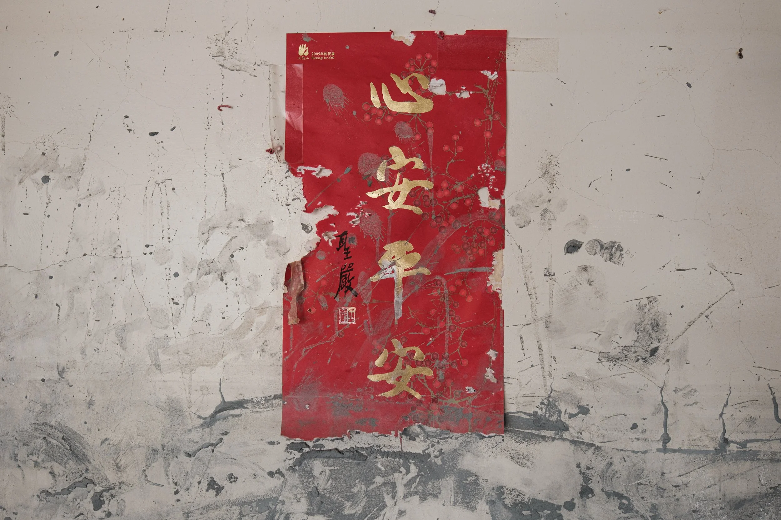 A red Lunar New Year decoration is on a wall in a home that was destroyed in the Guangfu flooding. It's torn and covered in mud. The gold Chinese characters say "peace within, safety without." 