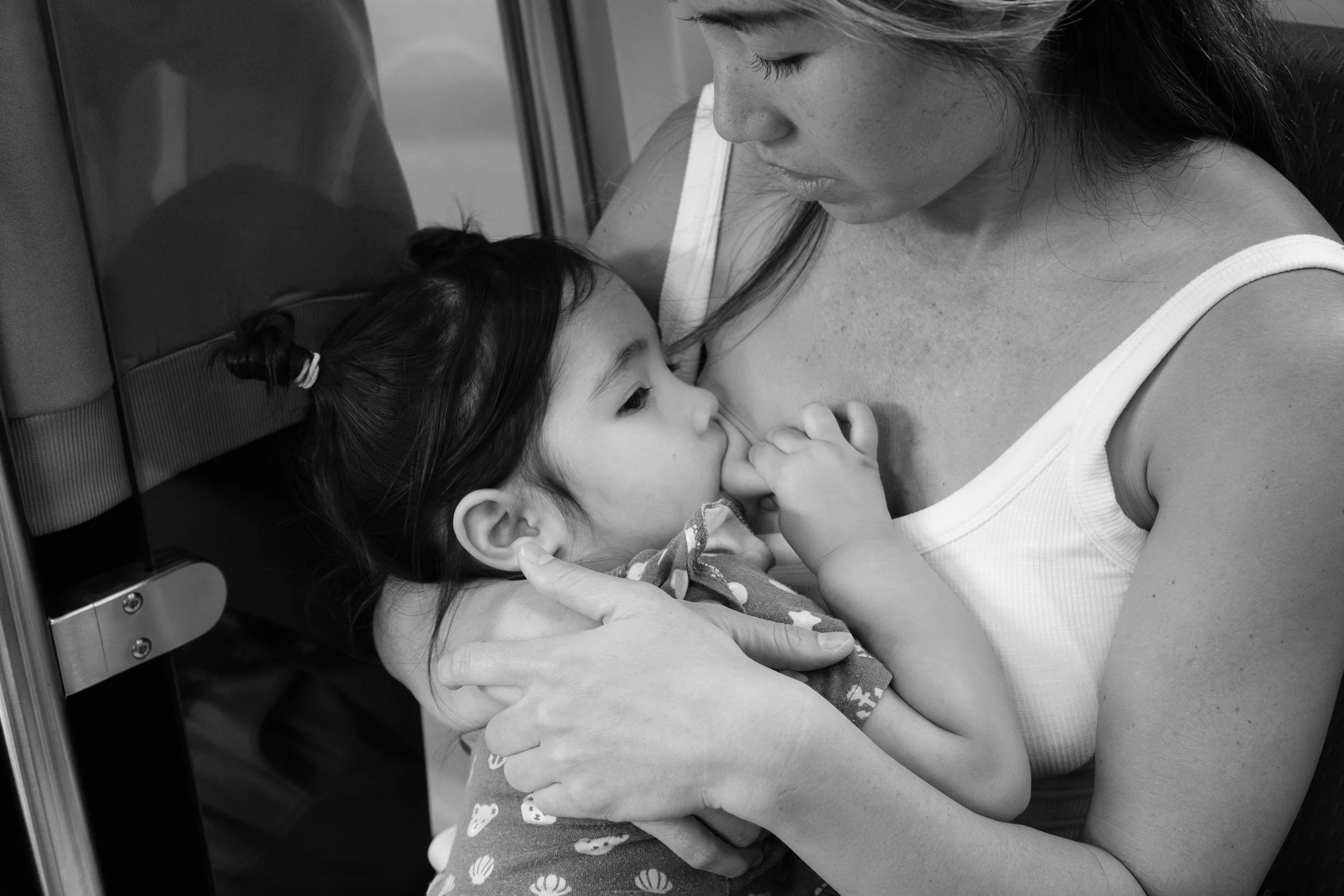 A toddler girl is squeezing her mother's breast as she nurses on a train going from Taipei to Yingge.