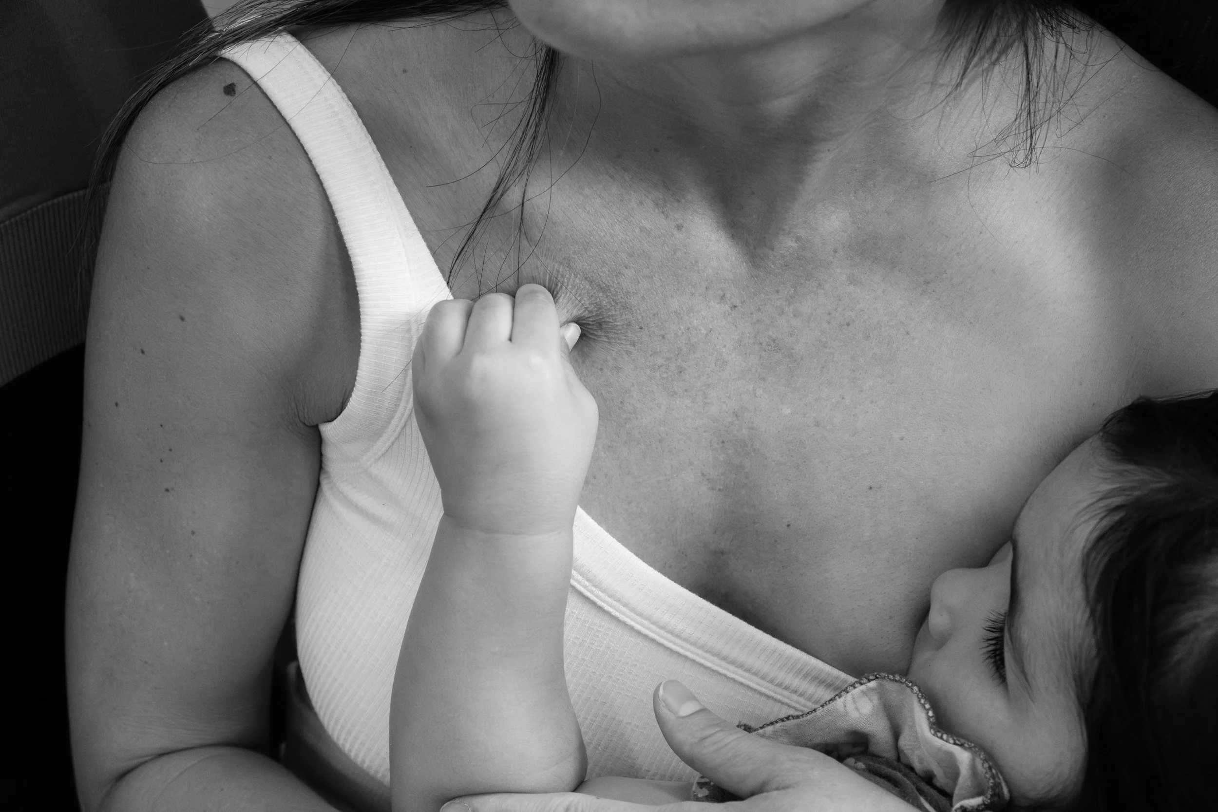 A toddler girl pinches the skin on her mom's chest as she breastfeeds on a train going from Taipei to Yingge.