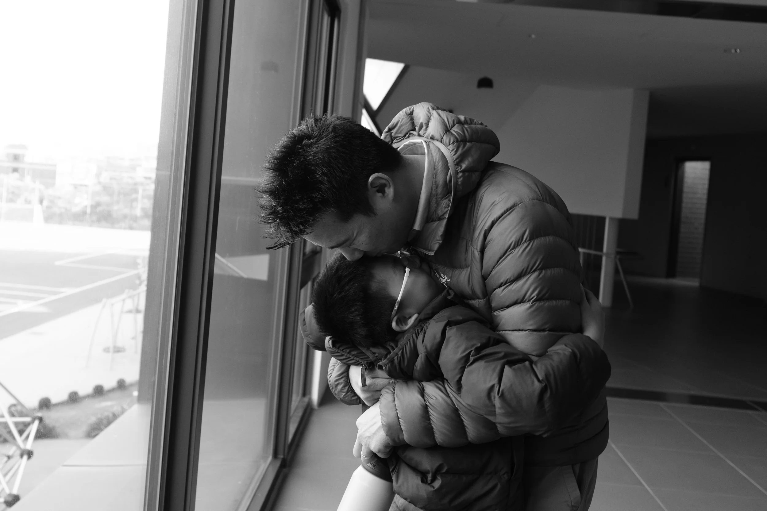 A father is bending over and kissing his son on the top of the head as he embraces him during a Taipei family photography session.