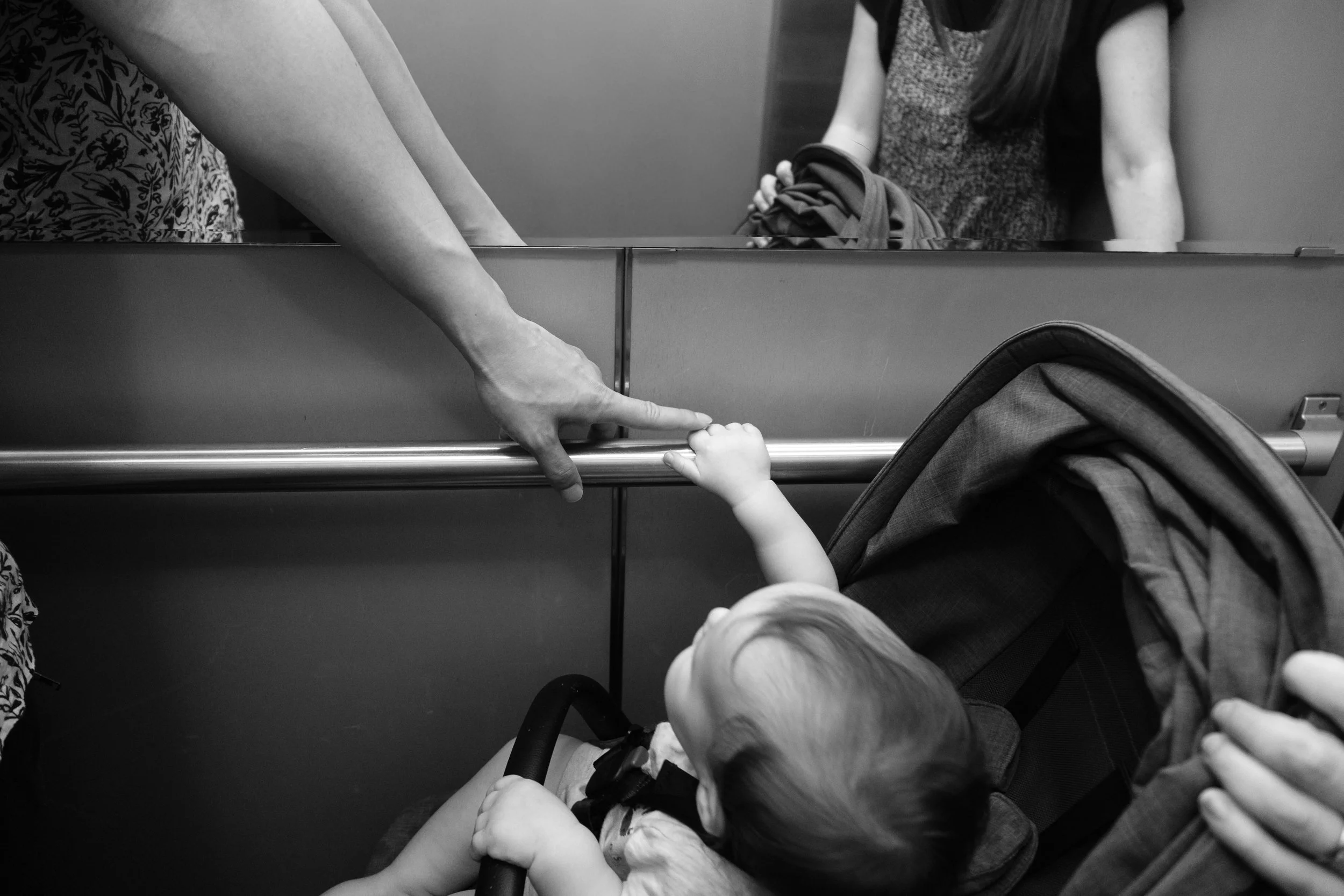A little boy is holind onto the railing in the elevator for their Taipei apartment building. His father is touching his hand with his finger.