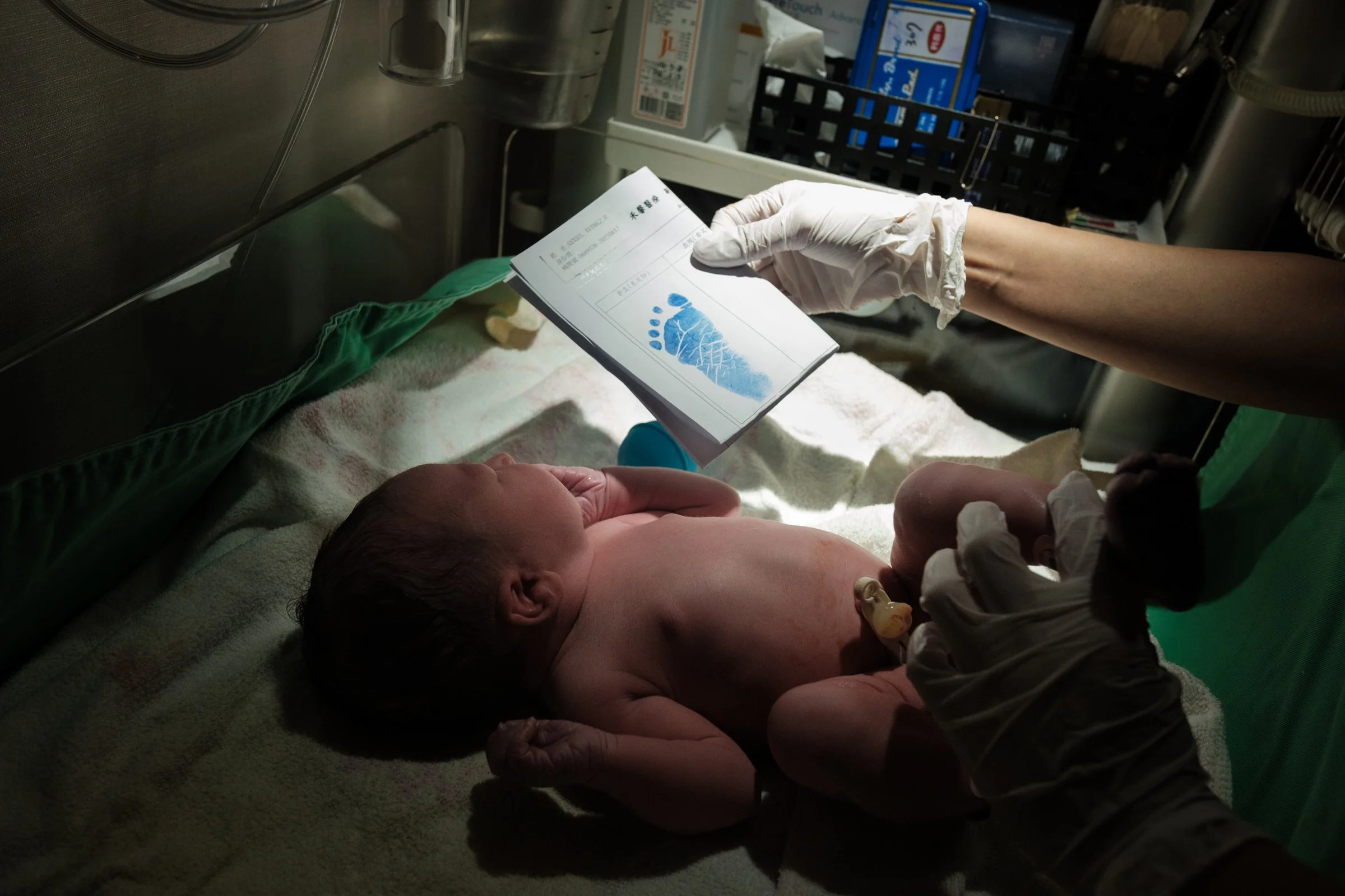 A color photo of a baby being weighed and getting her footprint done right after being born at Dianthus in Neihu. Photographed by Taipei birth photographer Cahleen Hudson.