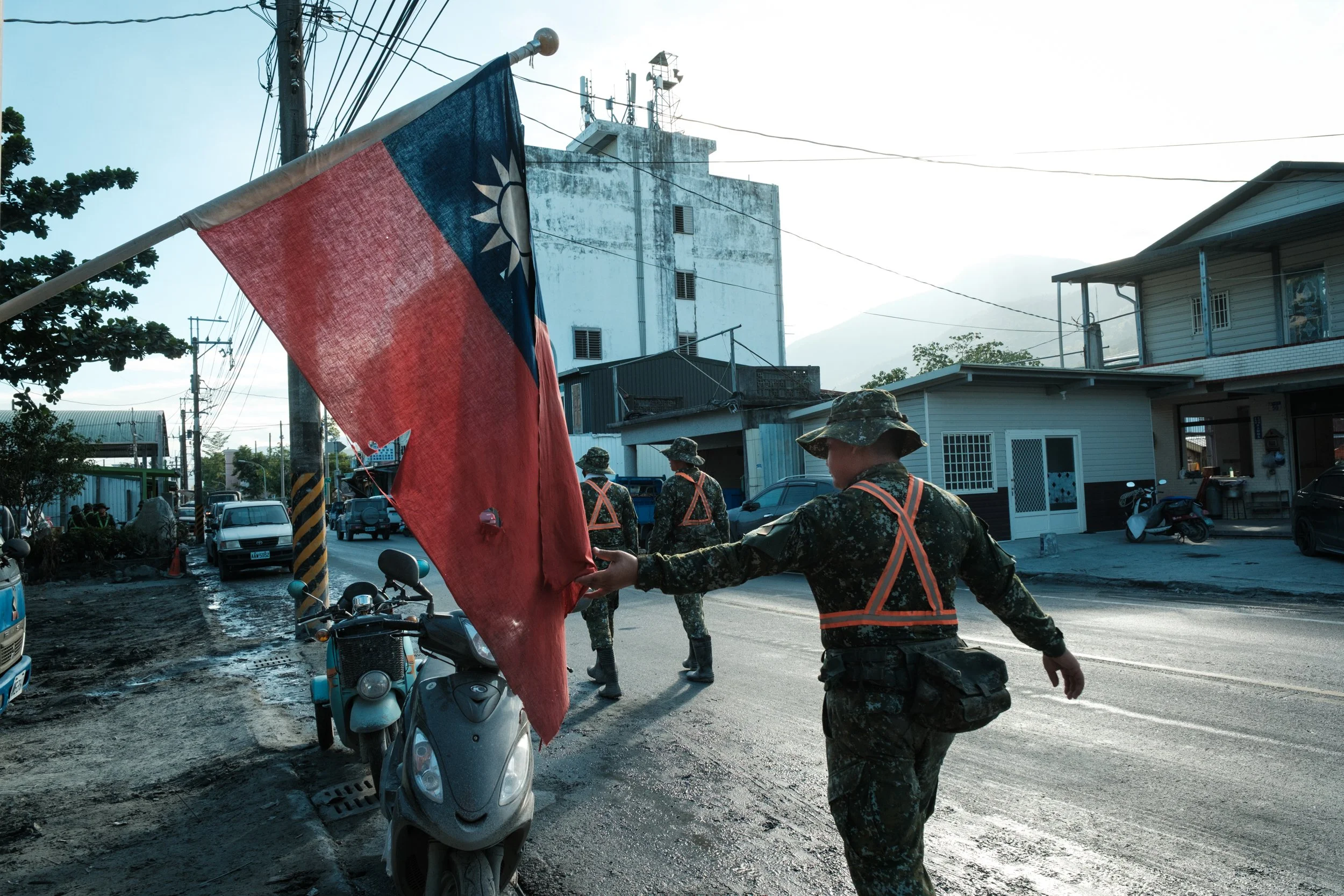 A Taiwanese soldier who has been sent to Guangfu to aid in the flood recovery efforts touches the Taiwanese flag as he passes by. The flag is hanging from a building. 