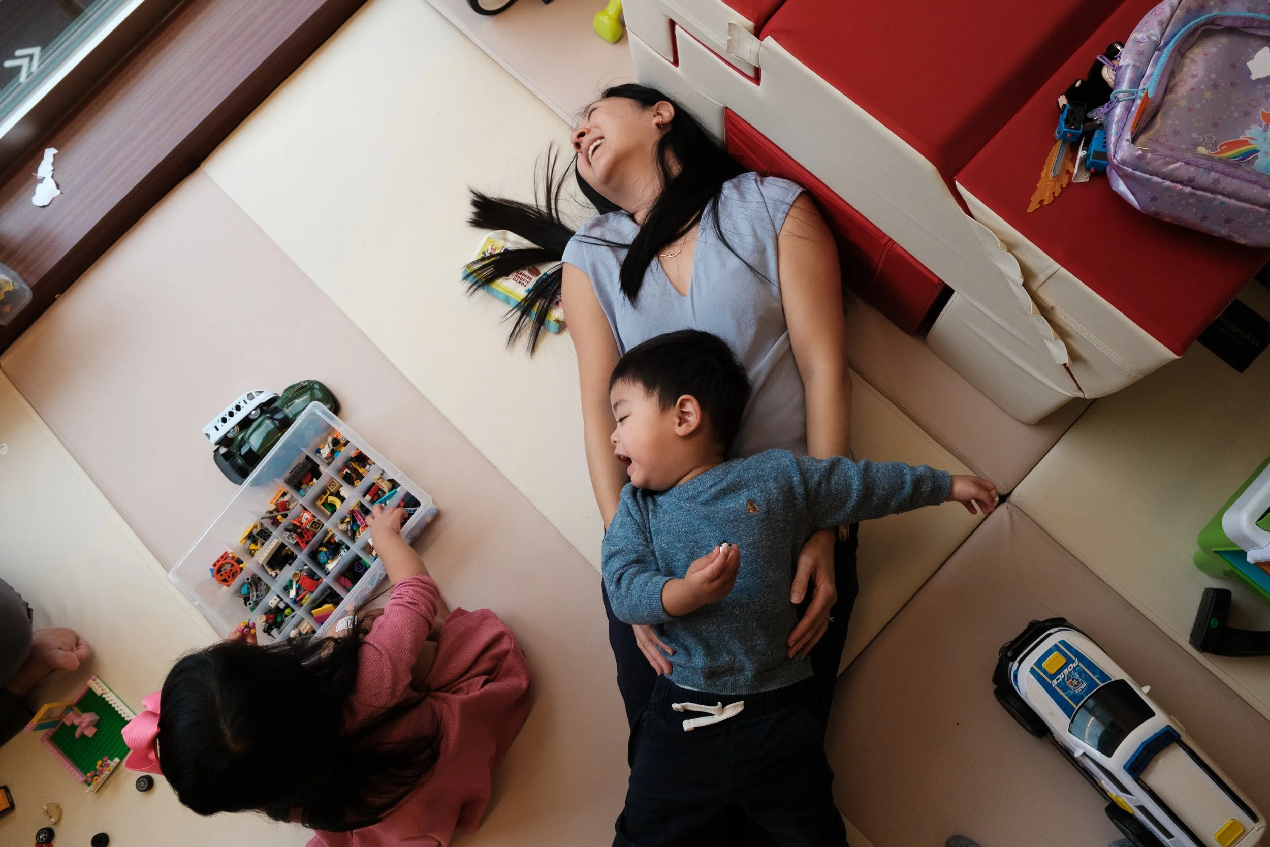 A woman is lying back on a play mat and laughing as she holds her little boy in a Taipei apartment.