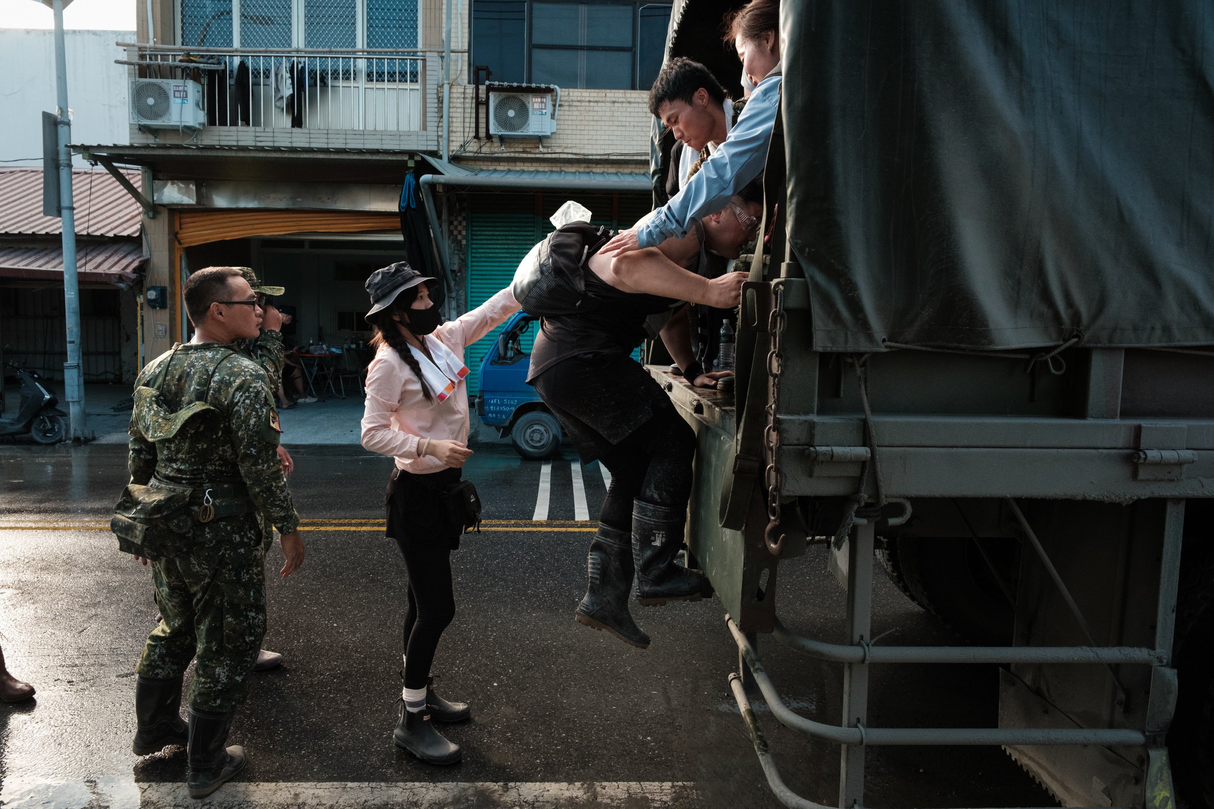 Volunteers are helping one another board a tall military truck in Guangfu Township, Taiwan. They are there to aid in the recovery efforts after a massive flood. 