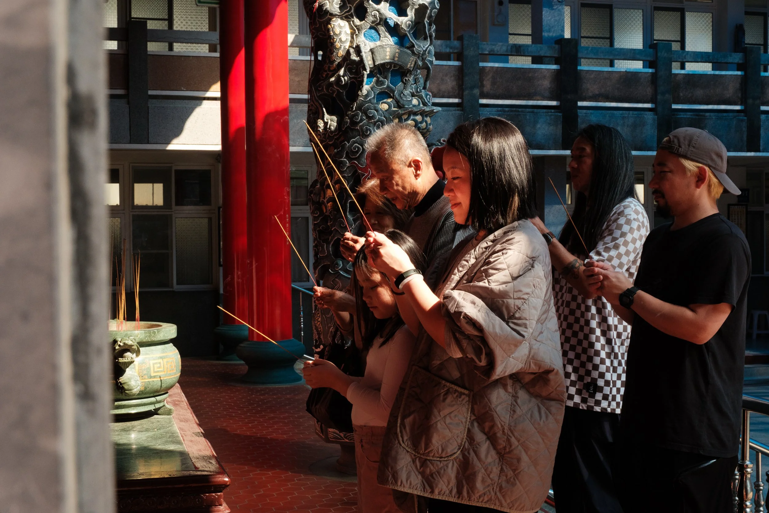 A family is lighting incense and bowing at an alter at a temple in Tainan during an outdoor family photoshoot.