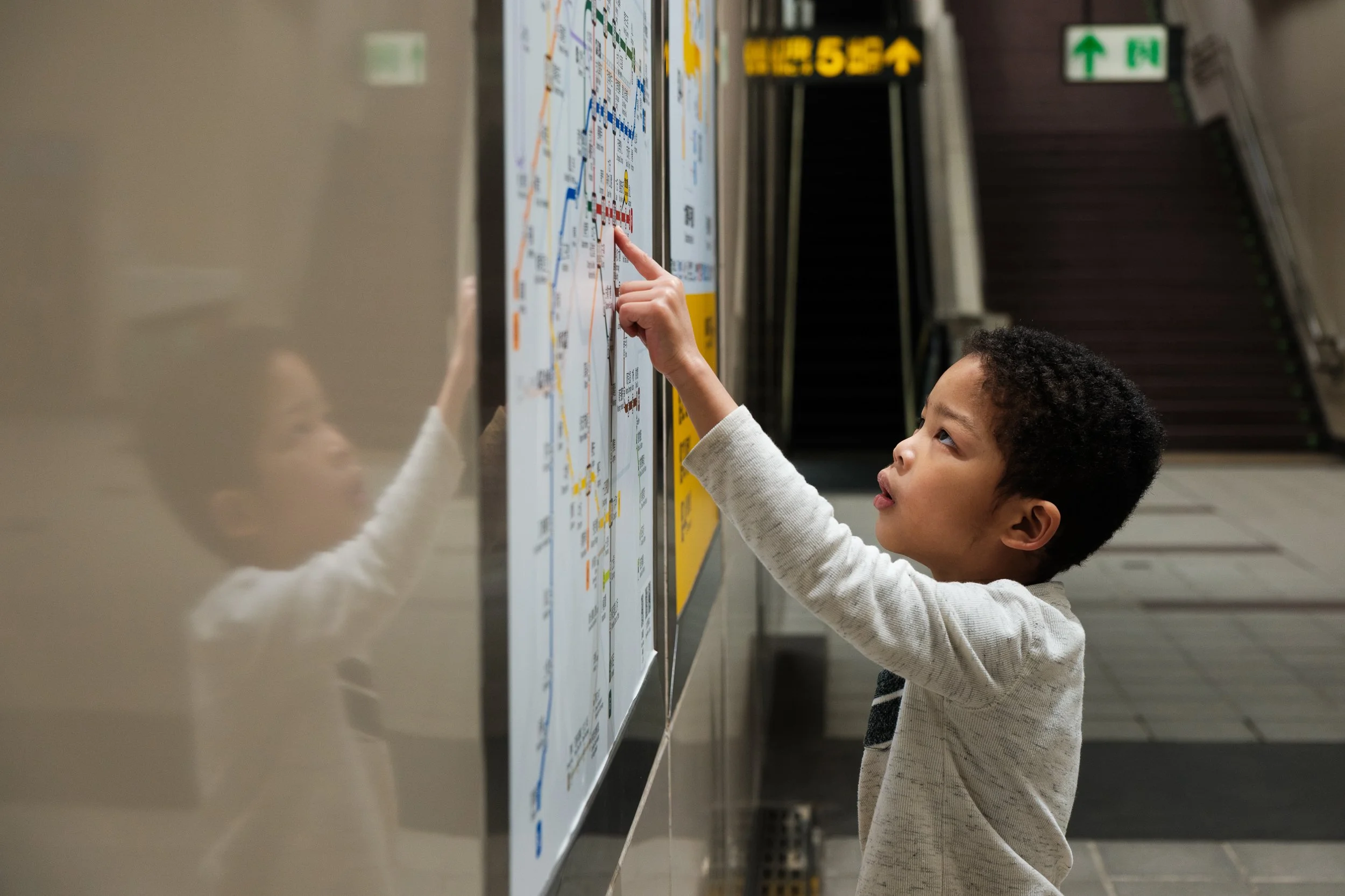 A young boy is carefully tracing a map in a Taipei MRT station with his finger. His reflection can be seen on the wall. Photographed during an outdoor family photoshoot.