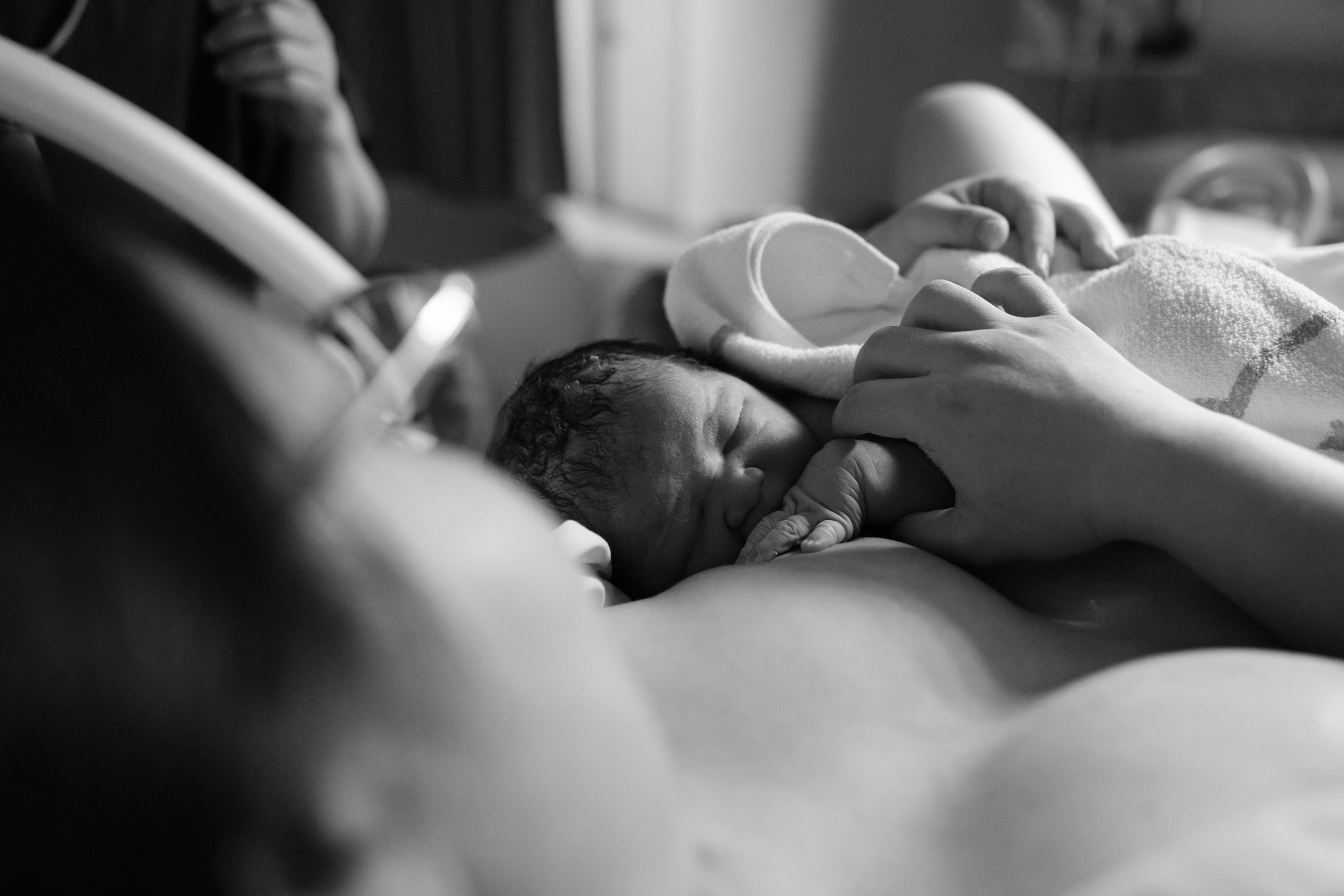 Black and white birth photography image of a newborn resting on their mother's chest at Dianthus, her hands gently holding the baby.