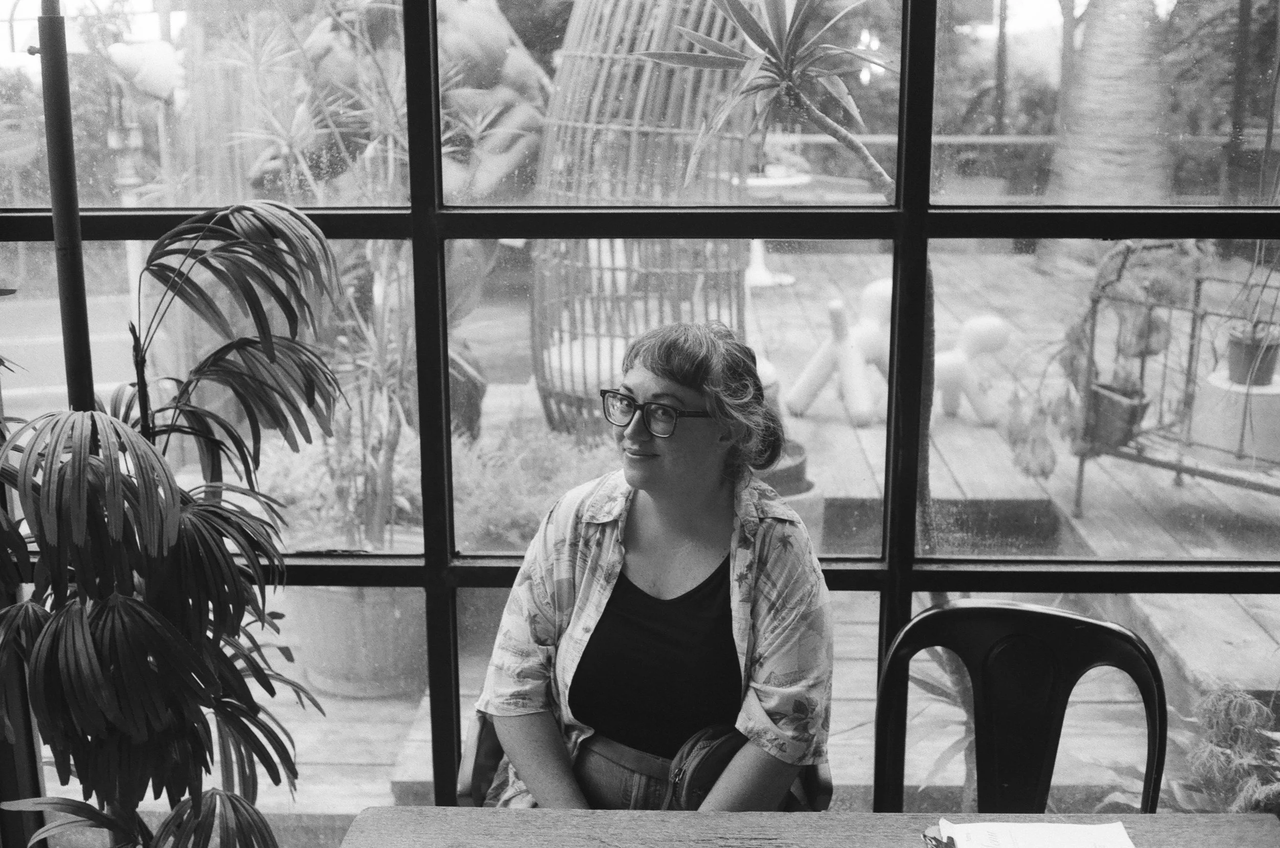 Taiwan photographer Cahleen Hudson is sitting at a table in a coffee shop in Taipei with a big window behind her. A luch garden can be seen through the window.