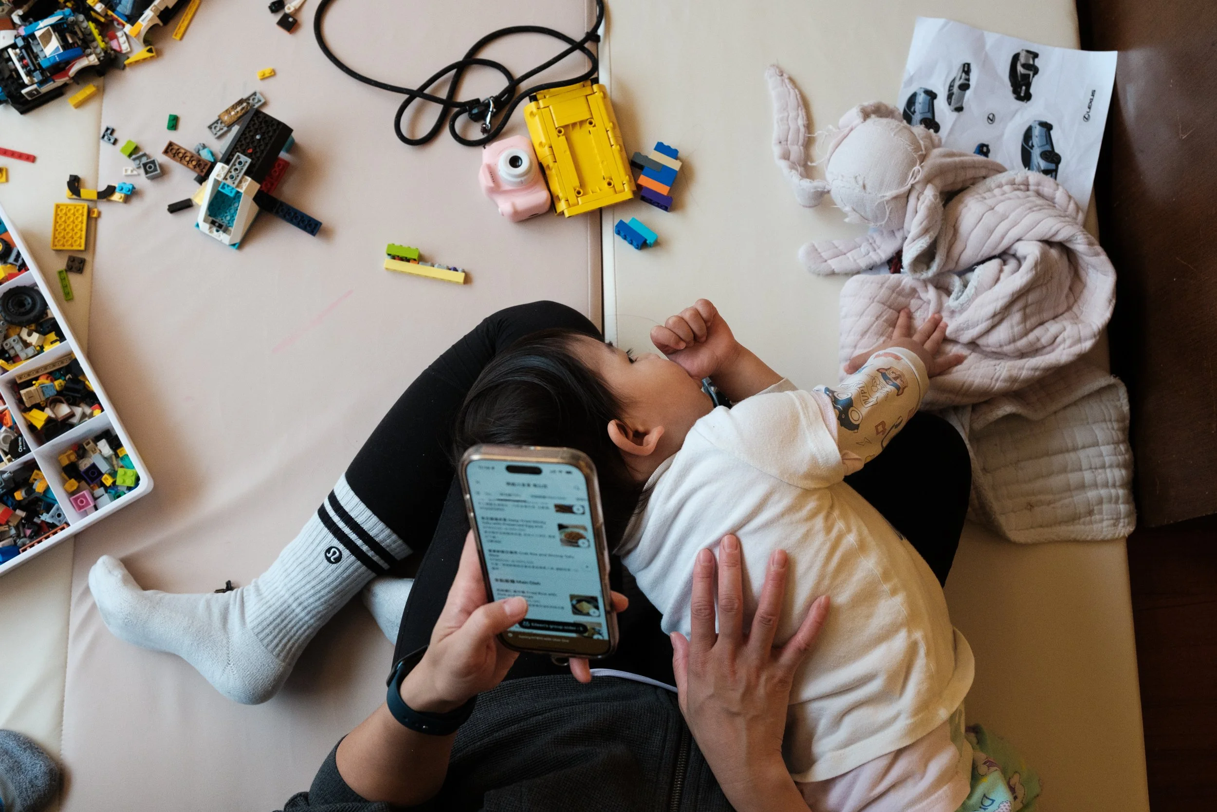 A woman is trying to order food on UberEats as her daughter lies on her lap during a documentary family photography session in Taipei.