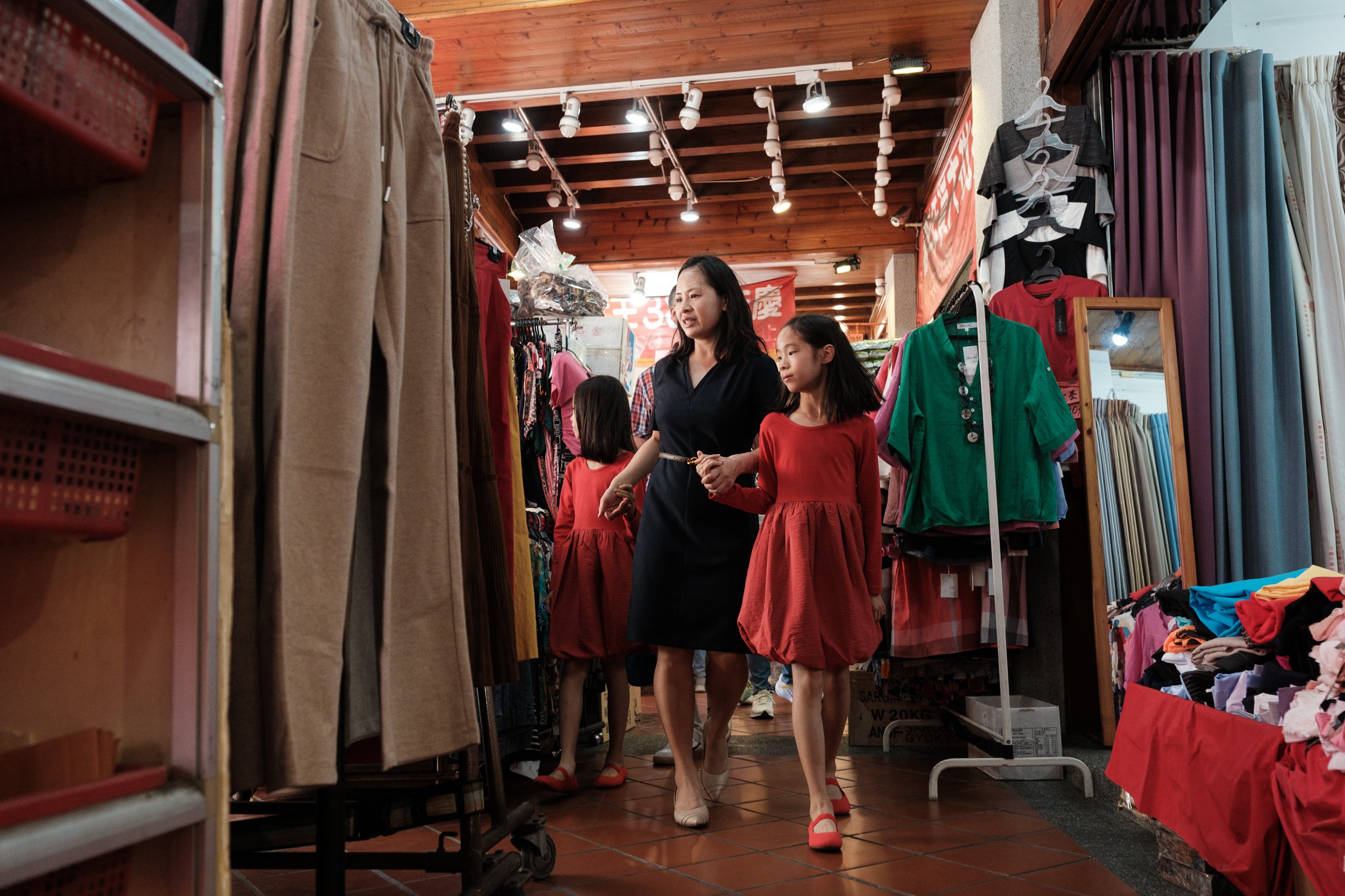 A color photo of a woman walking down Dihua Street with her twin daughters who are wearing matching red dresses. Photographed during an outdoor family photoshoot by Cahleen Hudson.