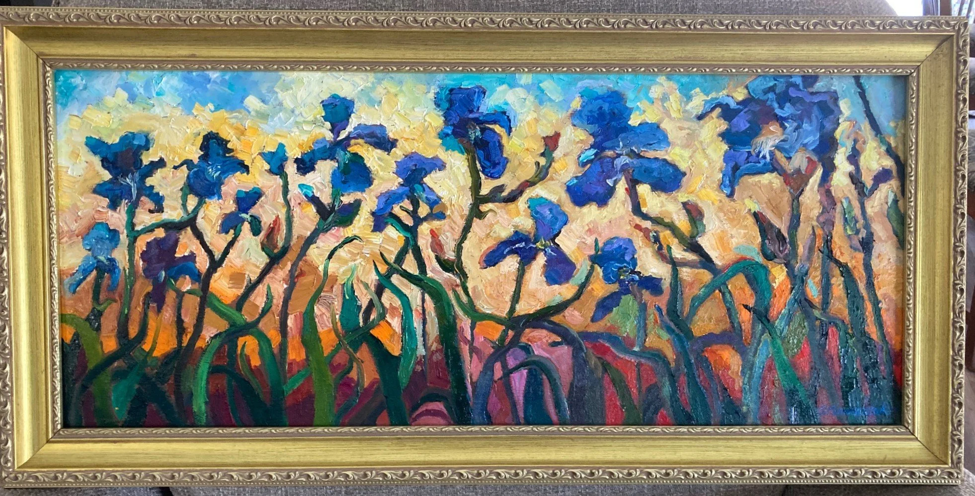 A colorful abstract painting of blue irises with green stems against a vibrant background, framed in an ornate gold frame.