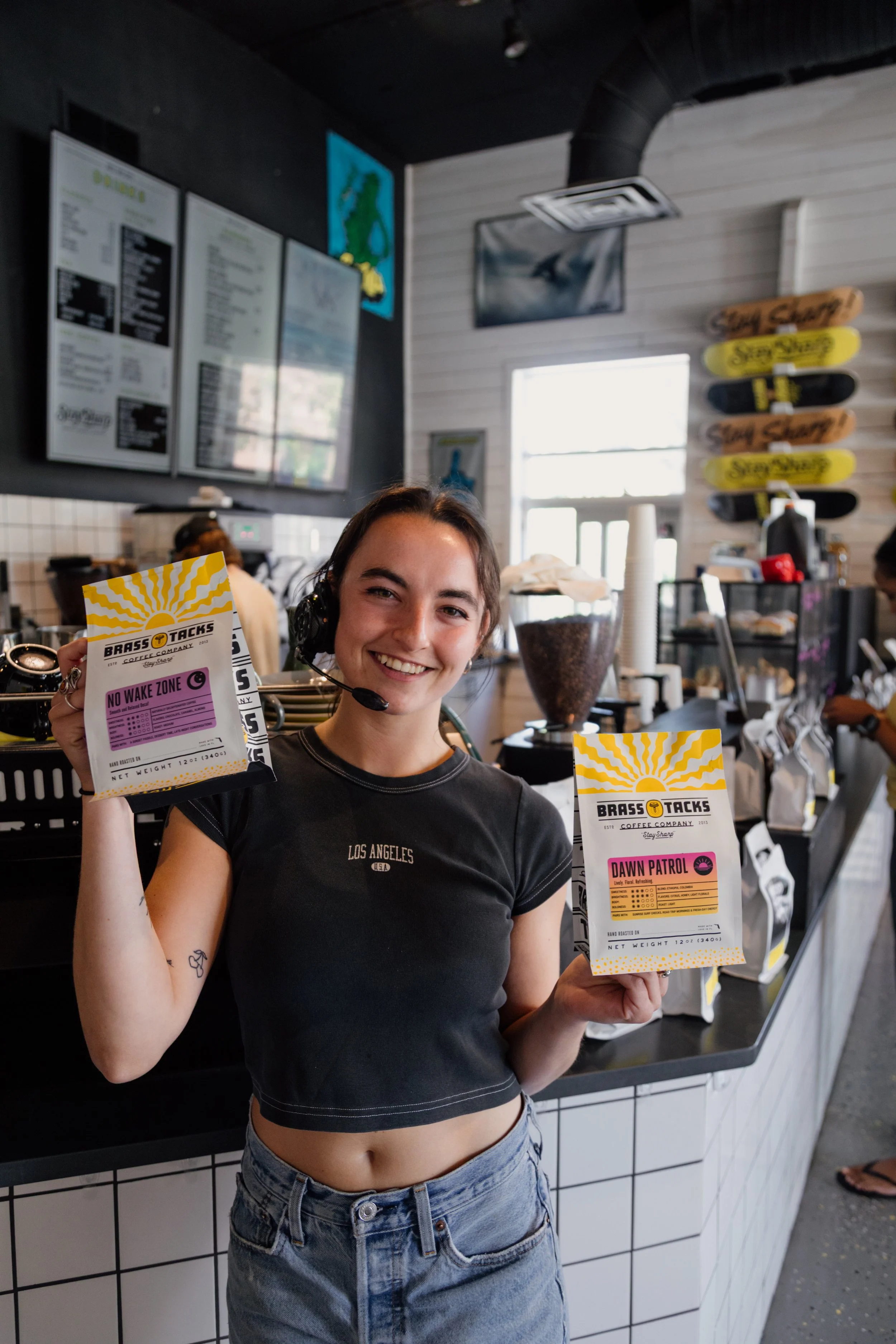 Barista Shainna standing in the Brass Tacks Southside cafe holding two bags of coffee