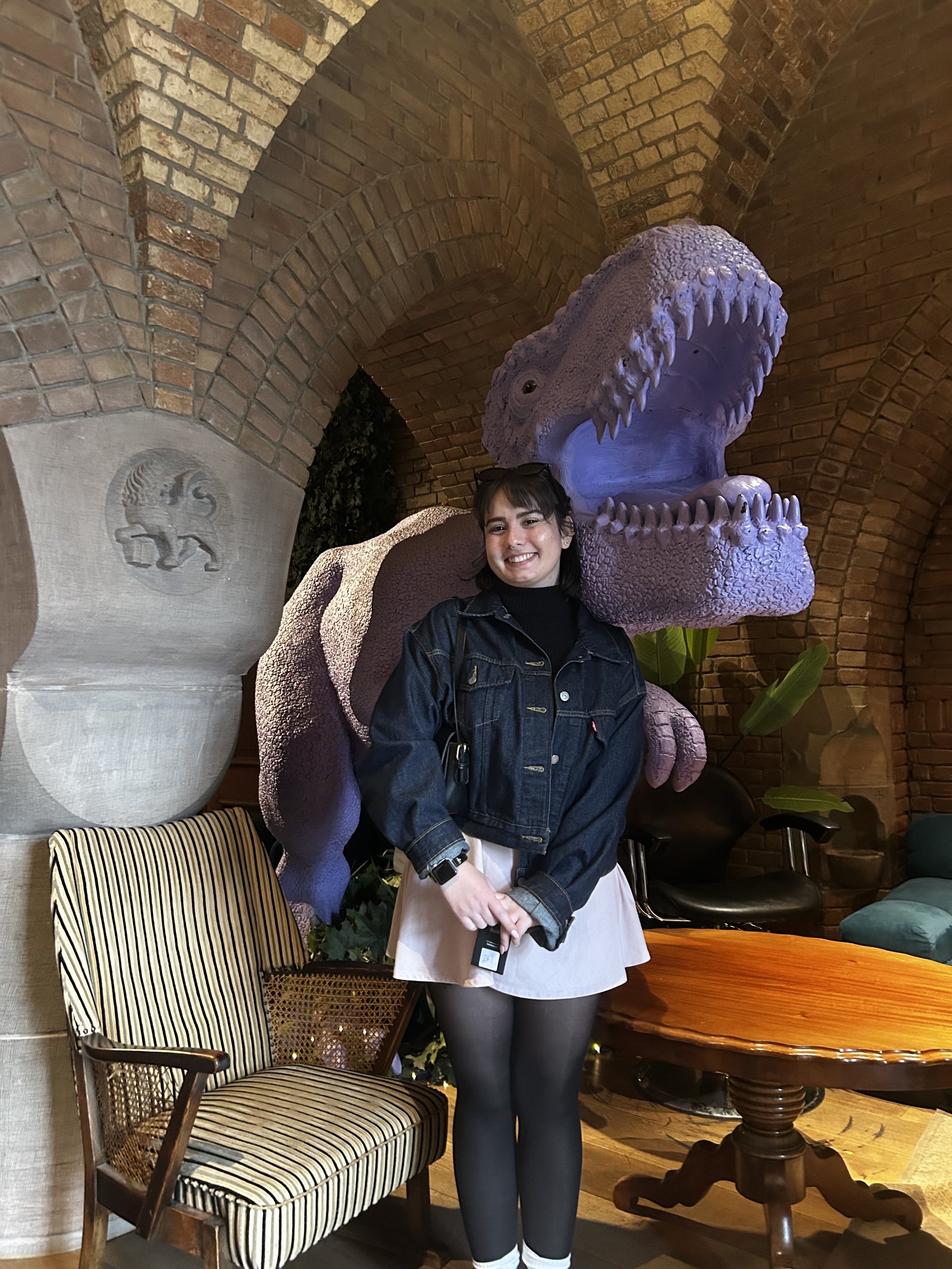 Anna, Fruit Cove Café Manager at Brass Tacks Coffee Co., smiling indoors next to a dinosaur display in a unique setting