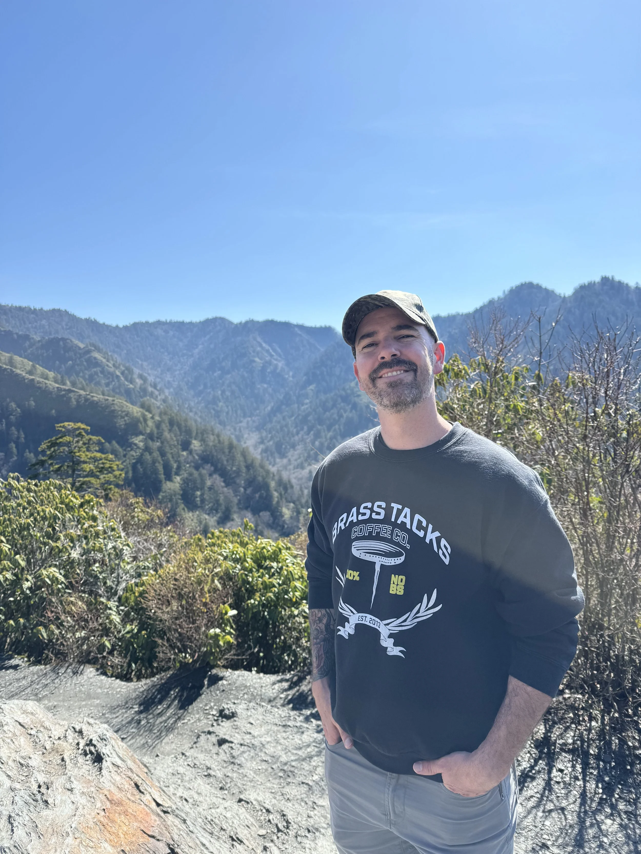 Steven, President of Brass Tacks Coffee Co., enjoying the outdoors in a mountain setting wearing Brass Tacks apparel
