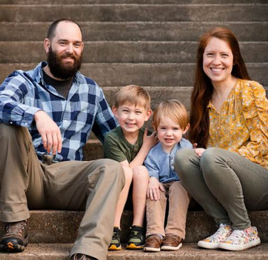 A happy family of four sitting on outdoor steps, smiling at the camera.