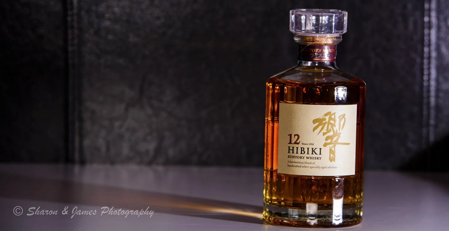 A bottle of Hibiki 12-year-old Suntory whisky on a table, casting a shadow to the left, with a dark textured background.