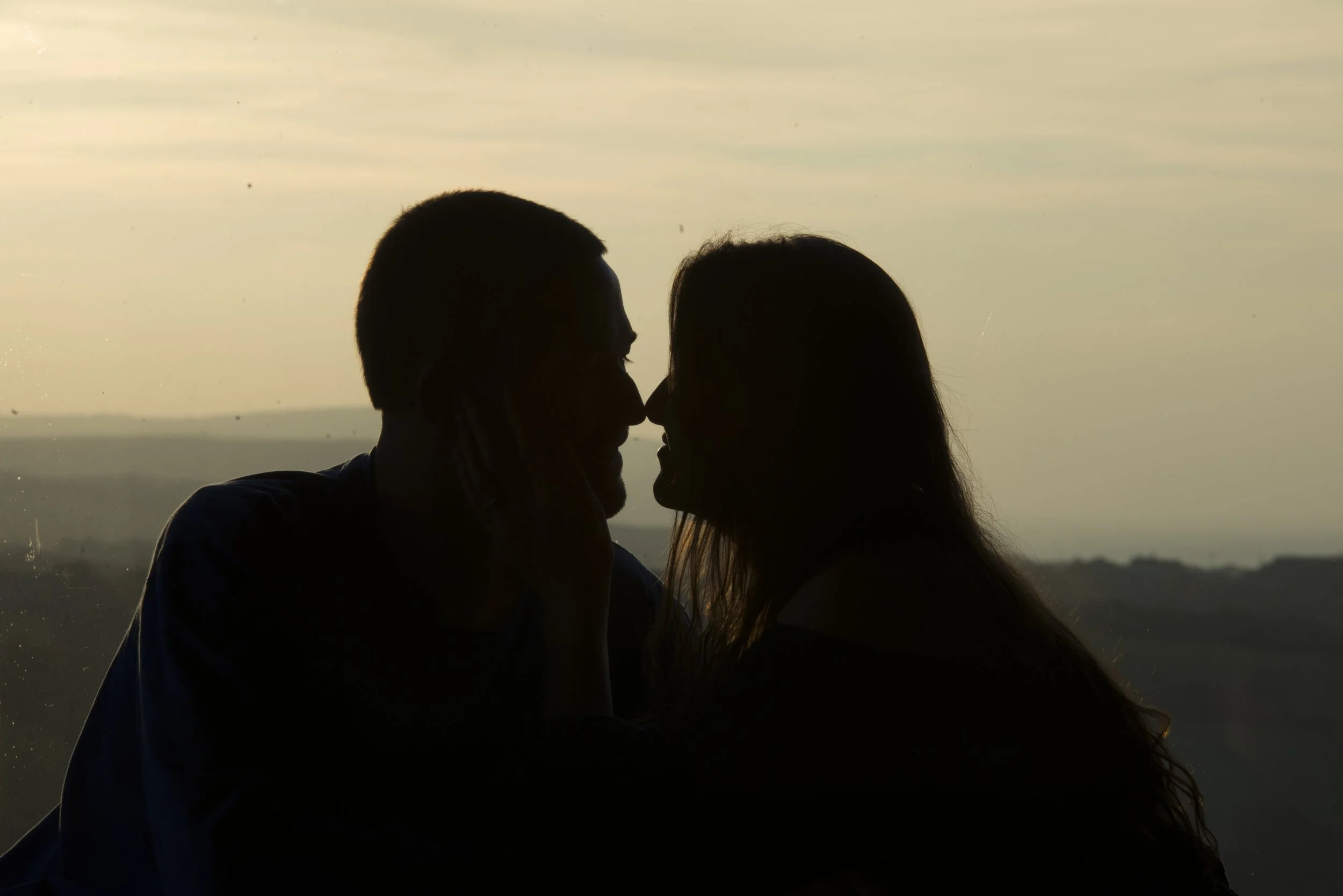 Silhouetted couple touching foreheads at sunset, landscape in background.