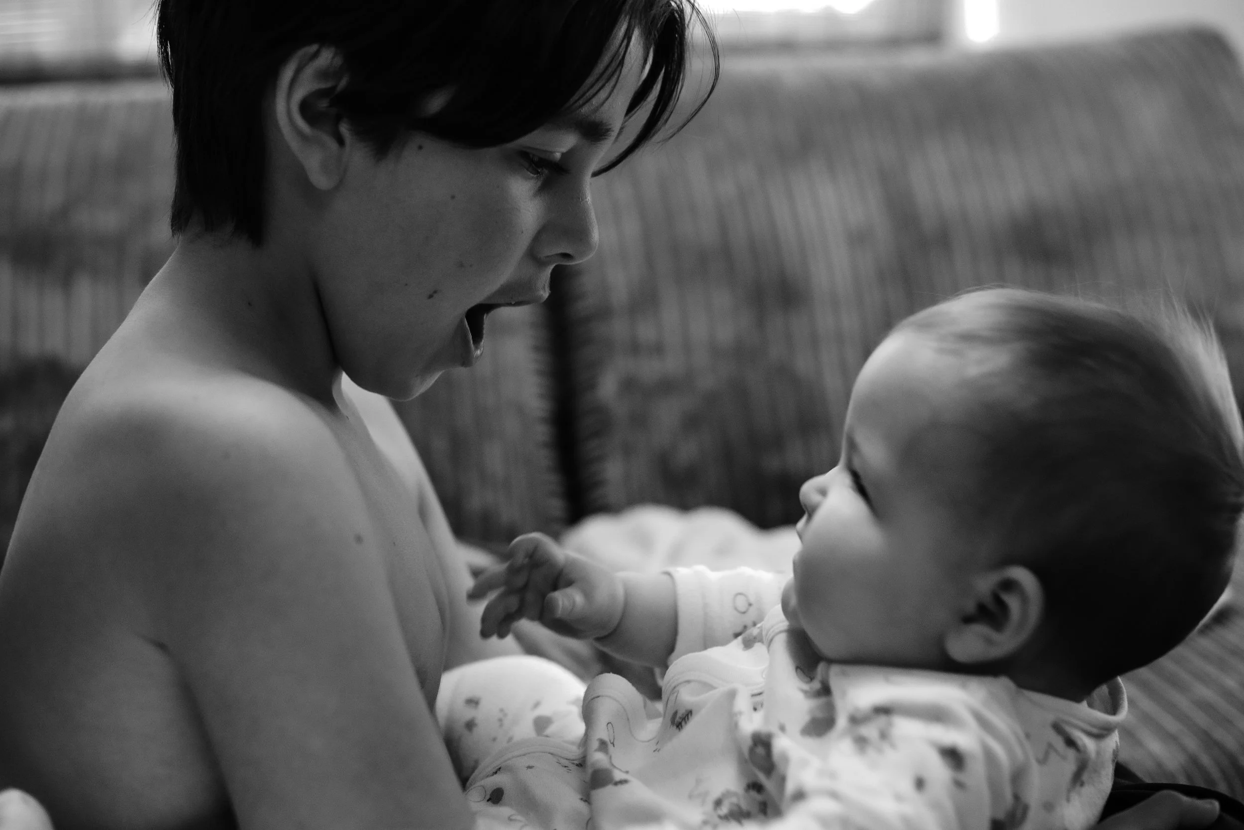 A black-and-white photo of a woman with short dark hair holding a sleeping baby with blond hair, both facing each other in an intimate moment.