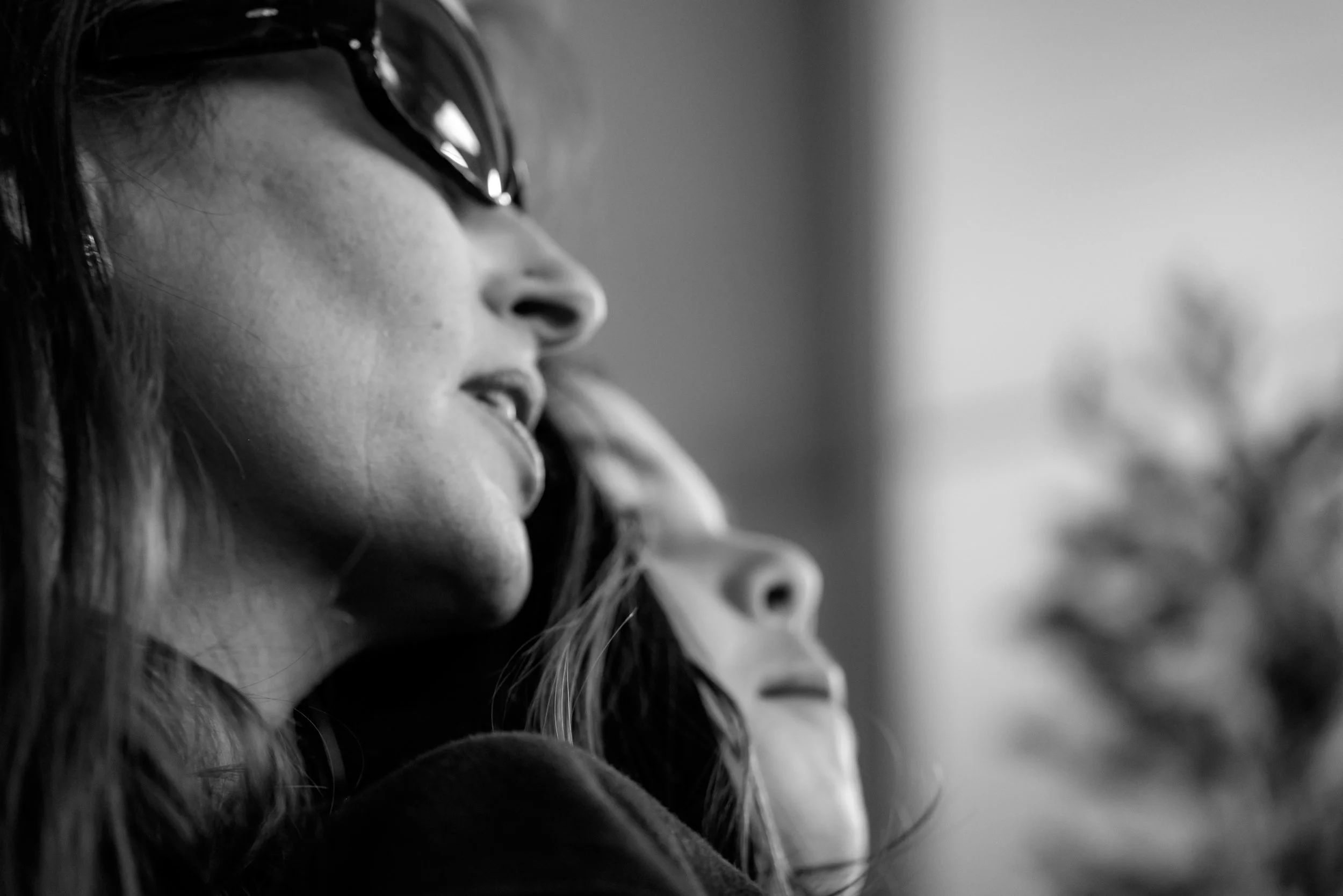 A close-up black and white photo of a woman with glasses, her face partially visible, showing her nose and lips, with long hair visible on the side.