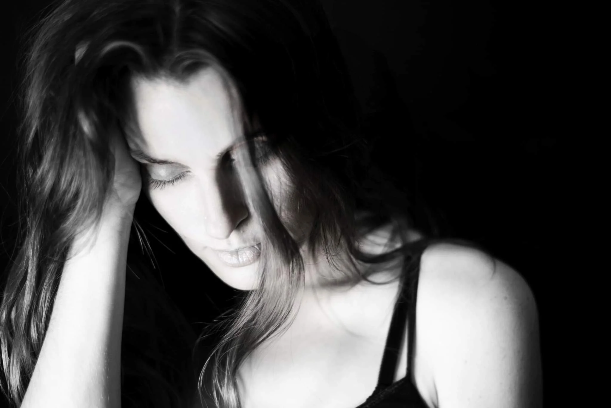 Black-and-white close-up of a woman with long hair, eyes closed, hand touching her face.