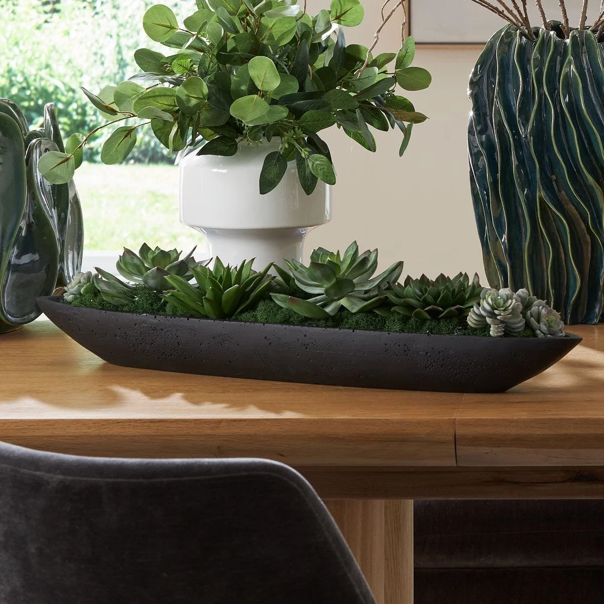 Lush faux succulents with preserved moss displayed in a long black stone planter