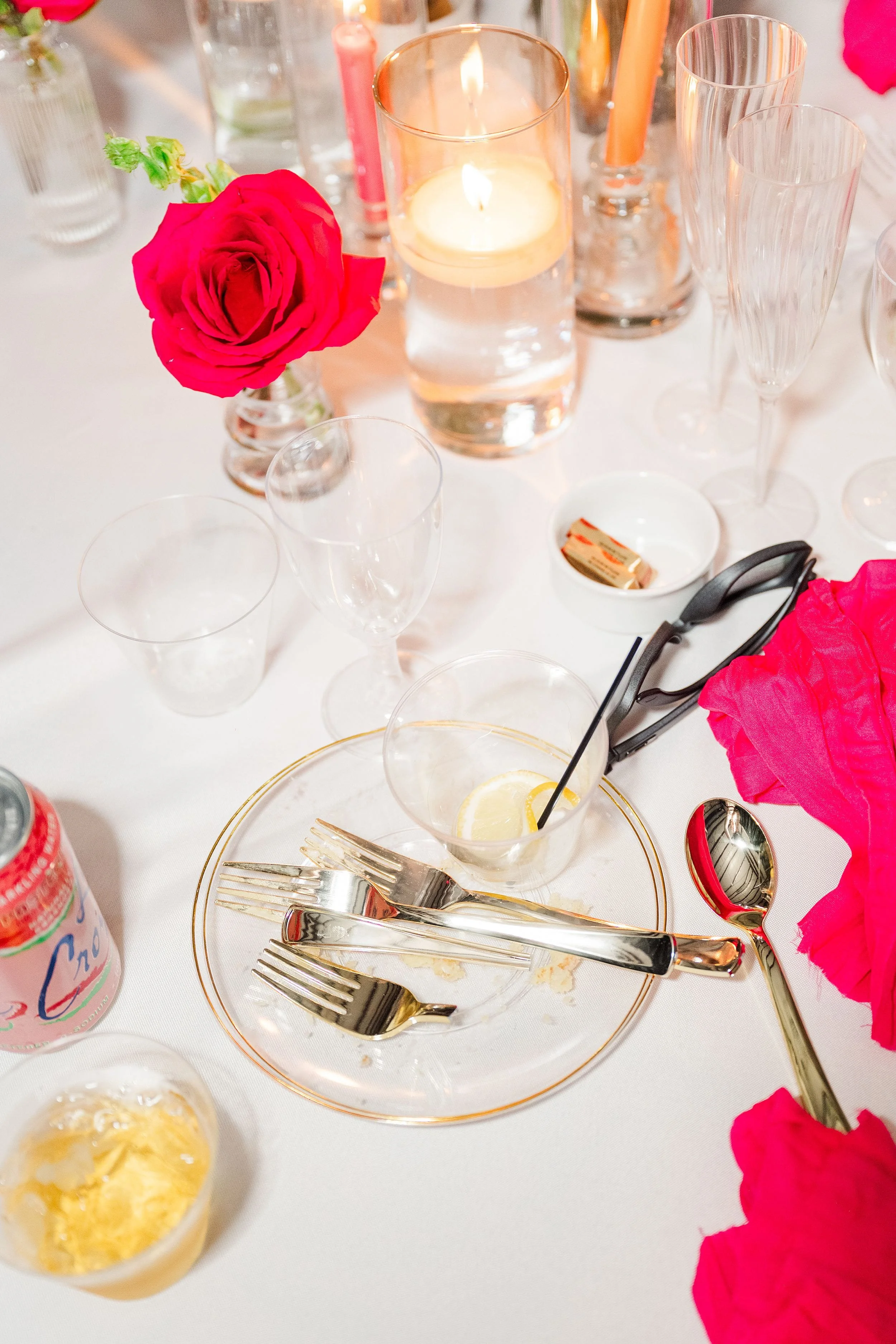 A table setting with bright red roses, glasses, and cutlery on a plate. A candle glows warmly, creating an elegant and festive atmosphere.