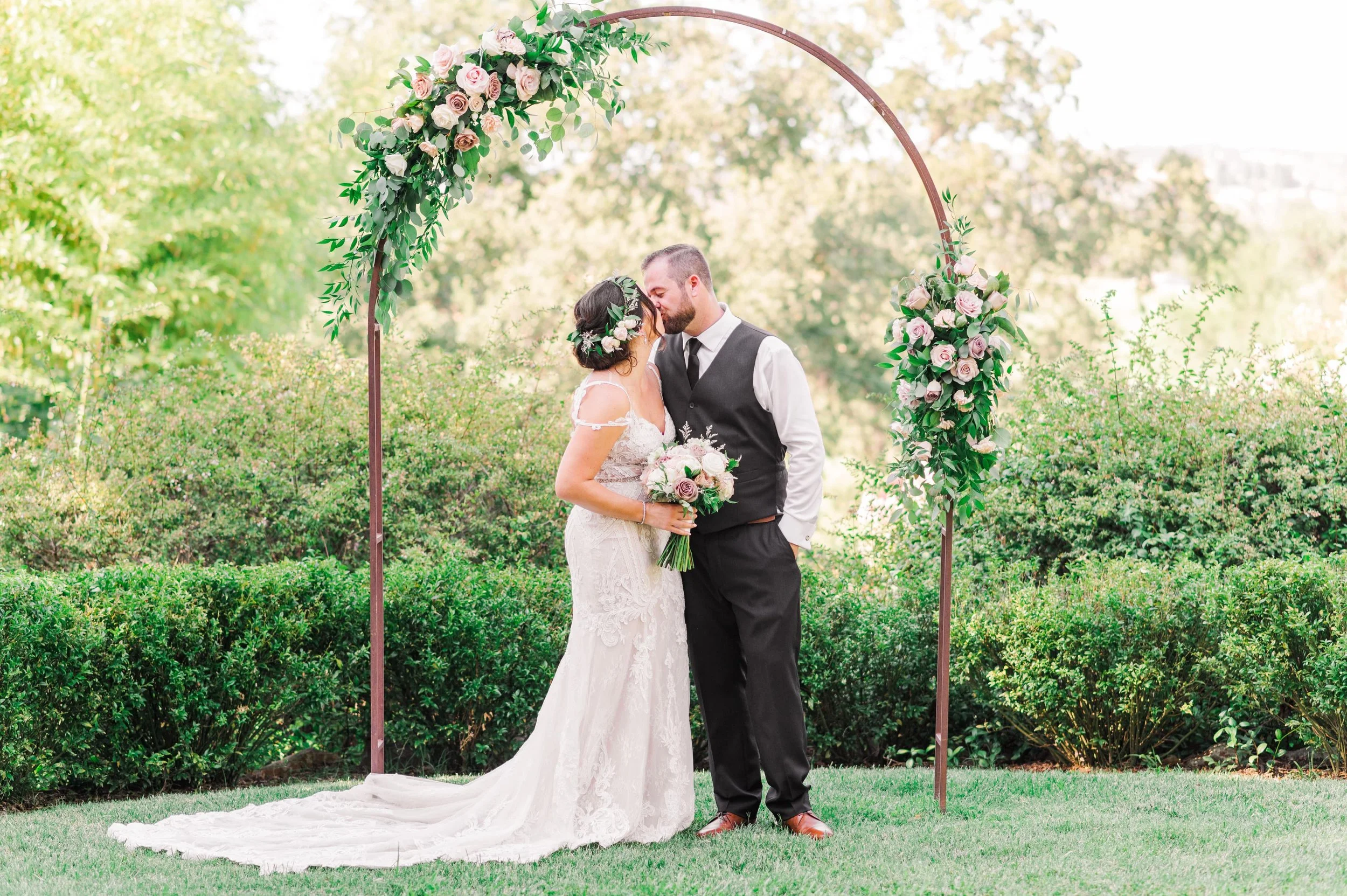 married couple sharing kiss under the wedding arbor at gold hill gardens newcastle california on hot summer day