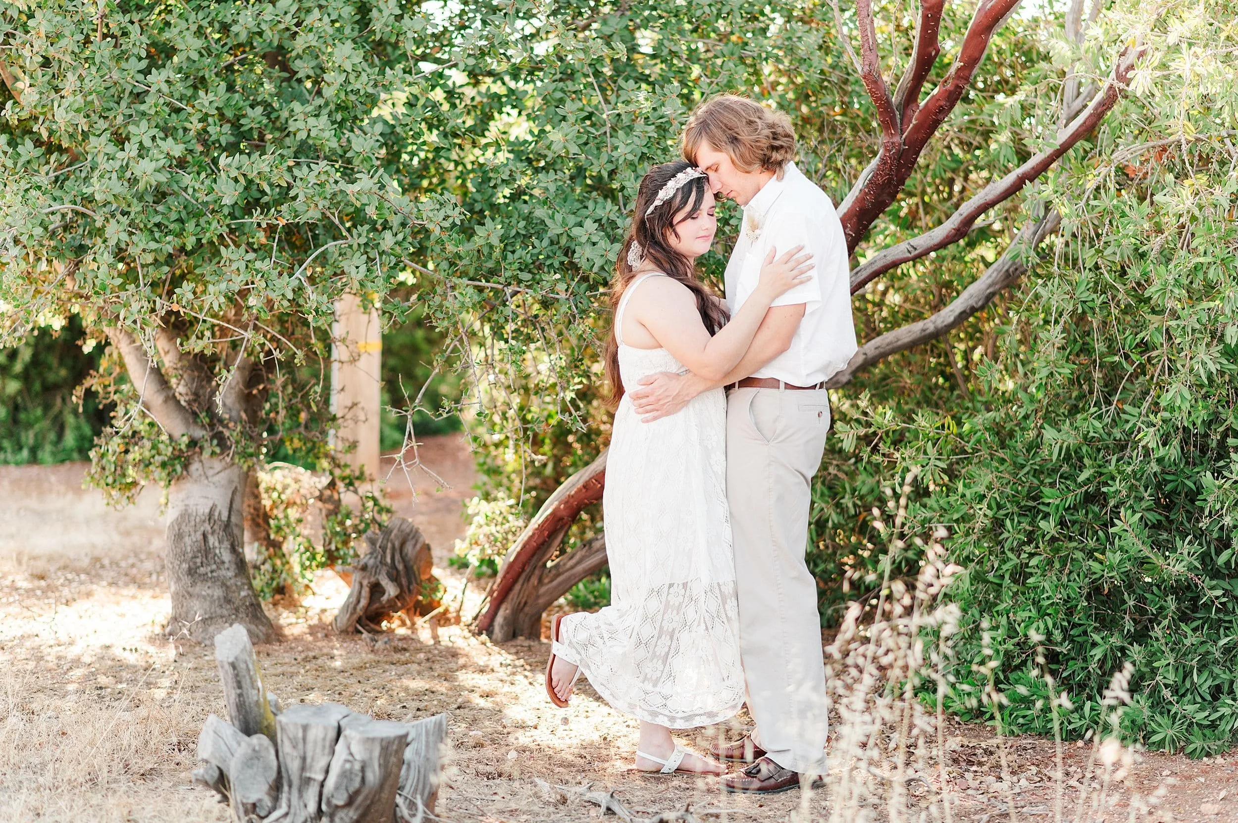 young engaged couple holding each other in front of manzanita tree