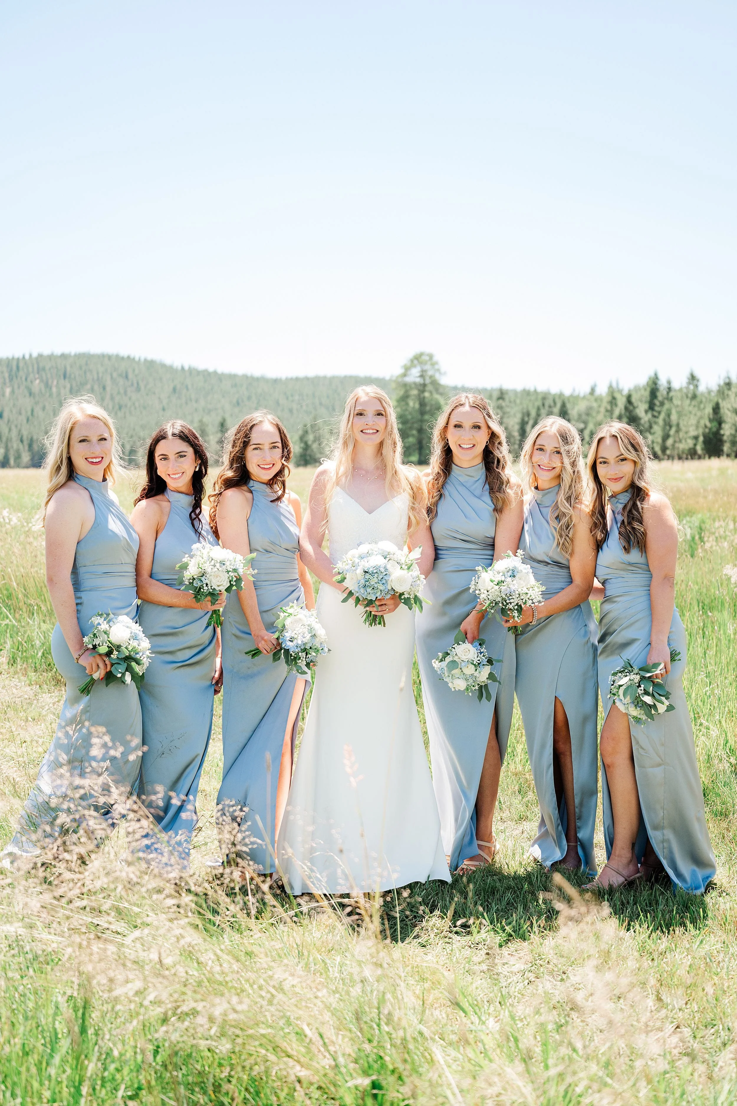Bridesmaids in blue dresses holding white and blue bouquets at a ranch wedding.