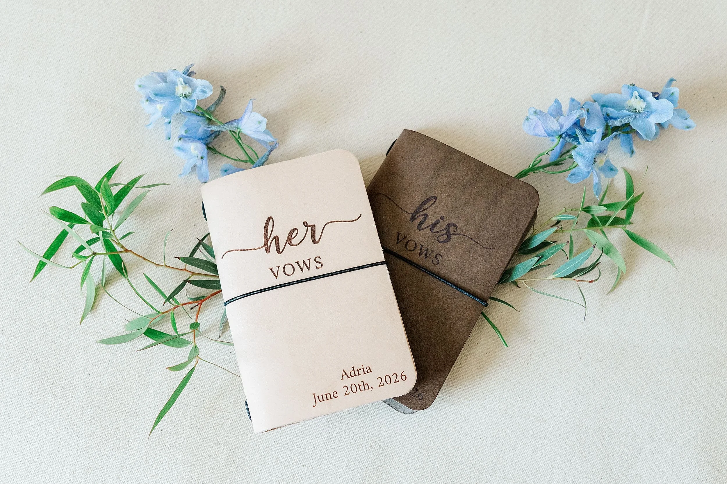 His and hers vow books styled with blue flowers and greenery.