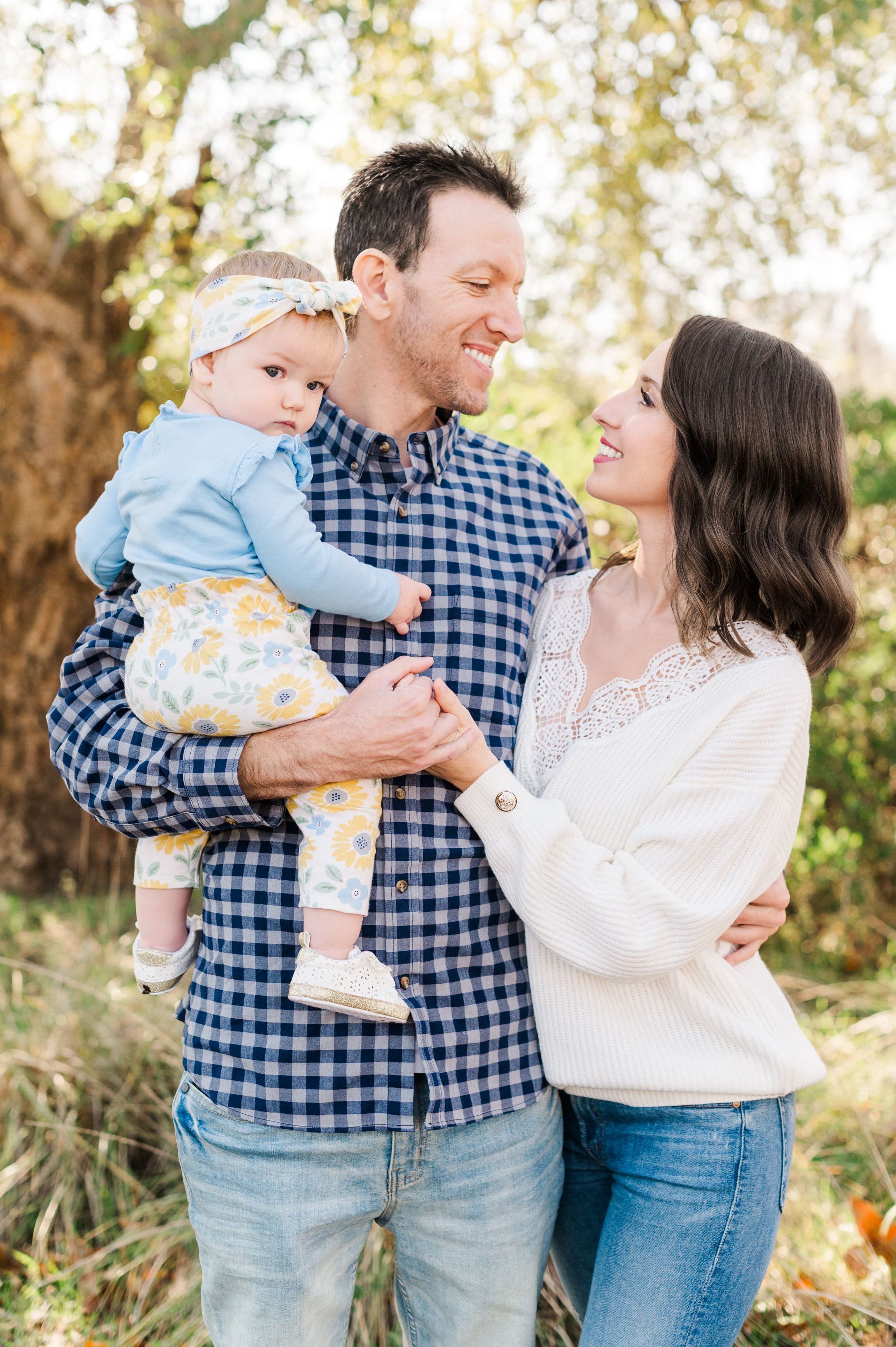parents smiling at each other holding hands while daddy is holding baby daughter