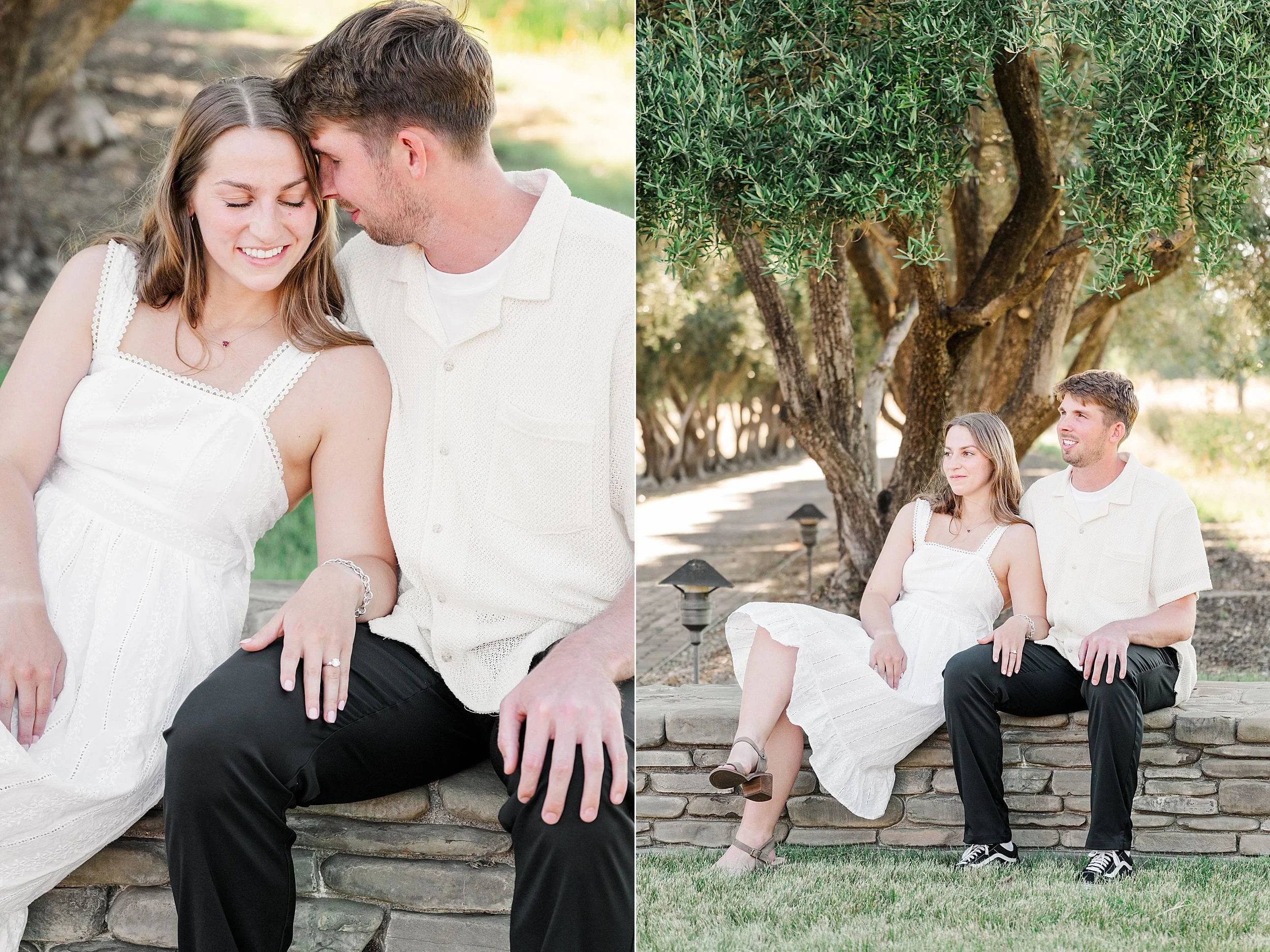 A couple sits closely together on a stone wall outdoors, both wearing light-colored outfits, with trees and grass in the background.