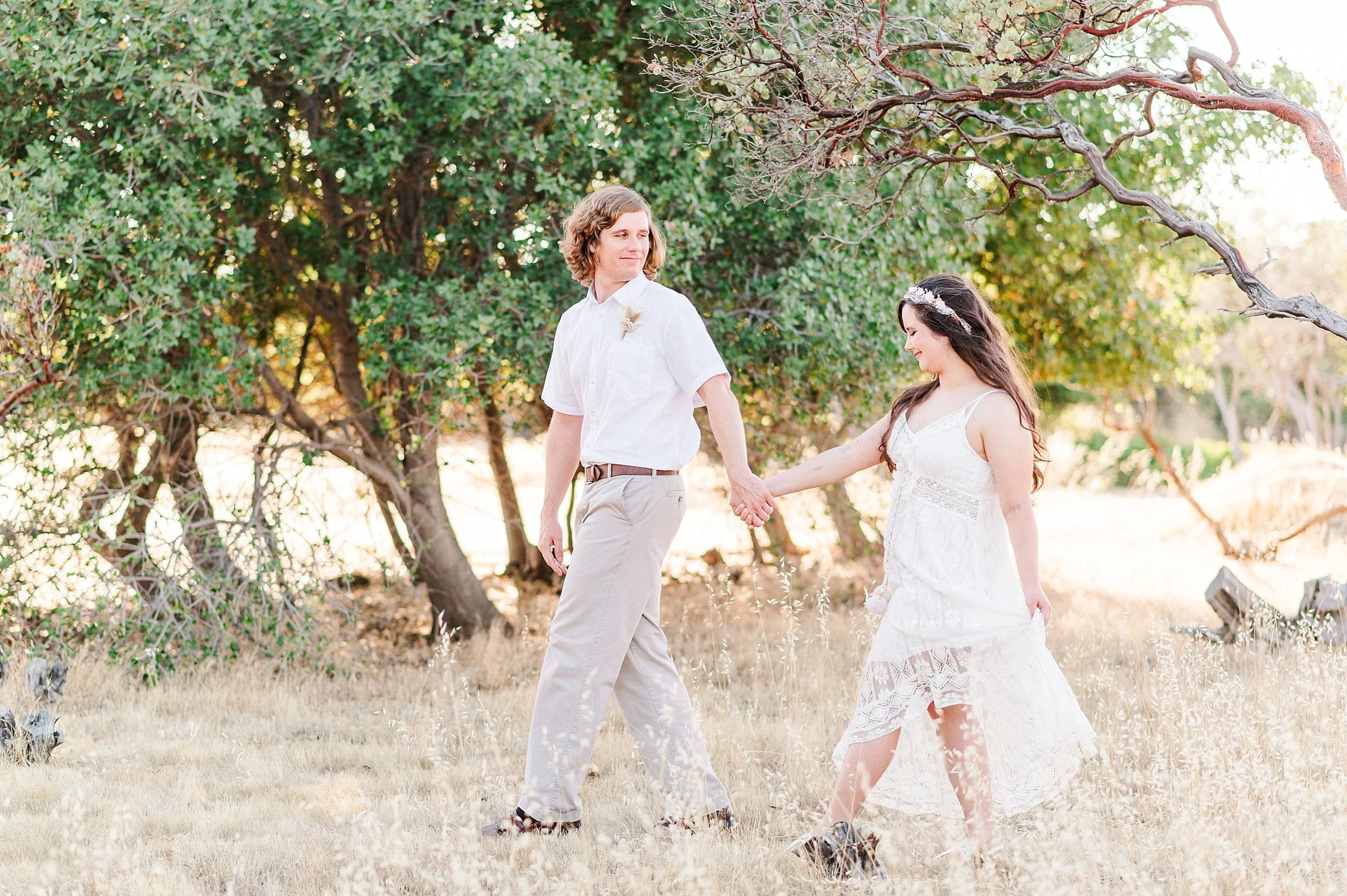 engaged couple walking away through dry grass