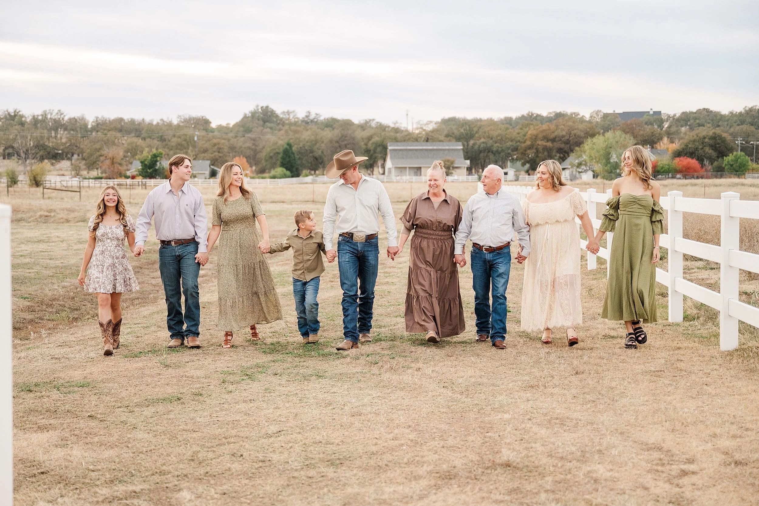 extended family walking together in field with white rail fencing