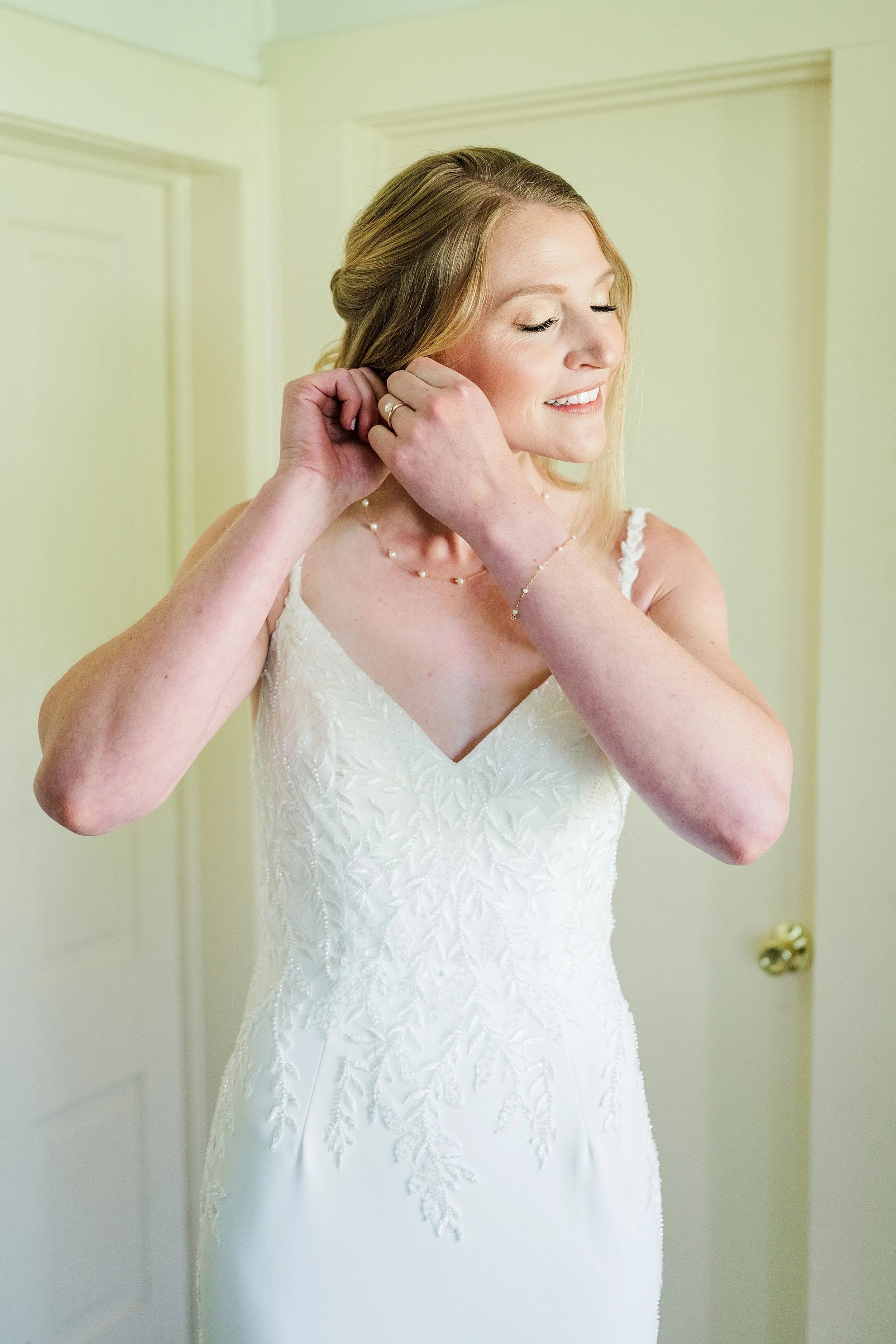 Bride putting on earrings in her wedding dress before the ceremony.