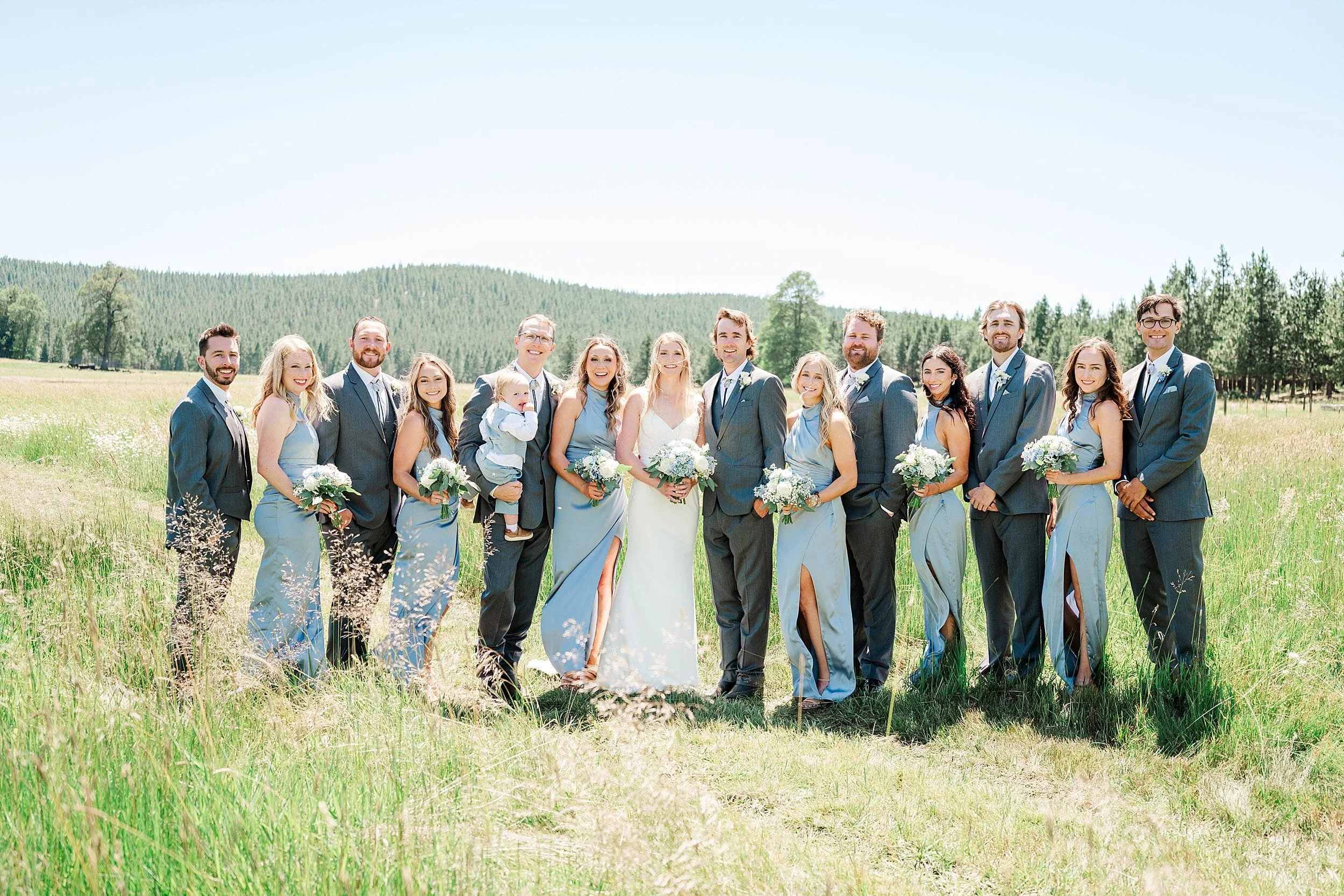 Wedding party portrait with blue bridesmaid dresses and mountain ranch scenery.